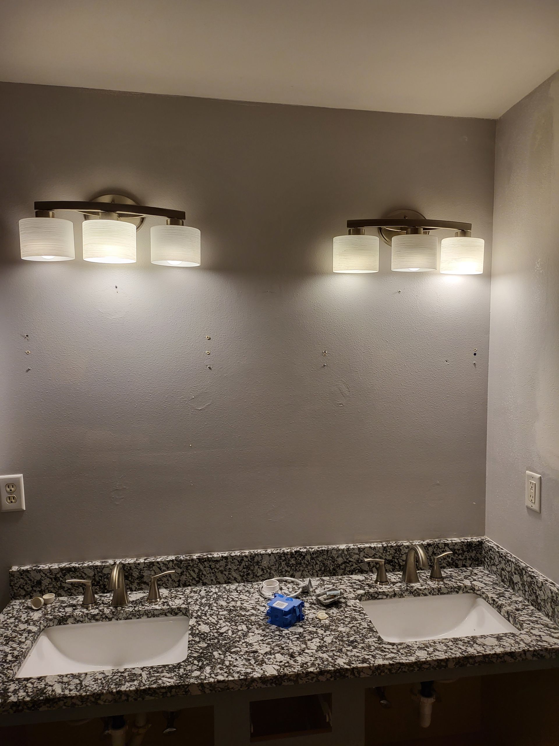 Bathroom vanity with two sinks, granite countertop, and wall lights above a large mirror