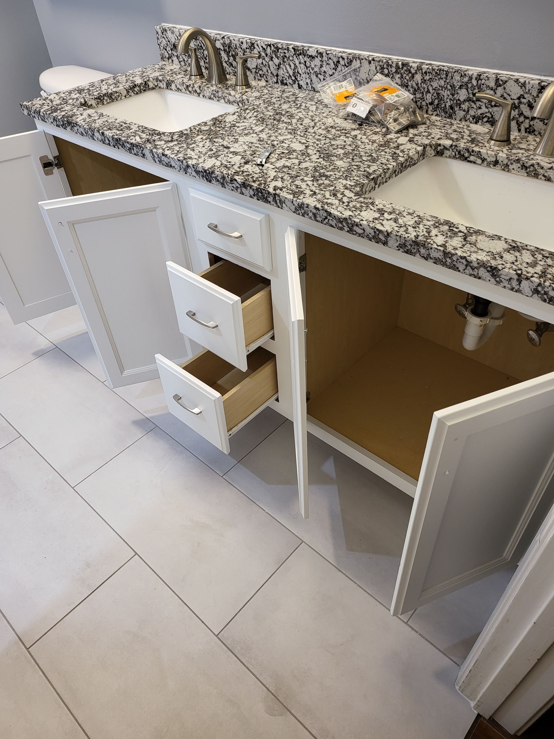 Kitchen vanity with granite countertop, sink, open cabinet, and two drawers pulled out.