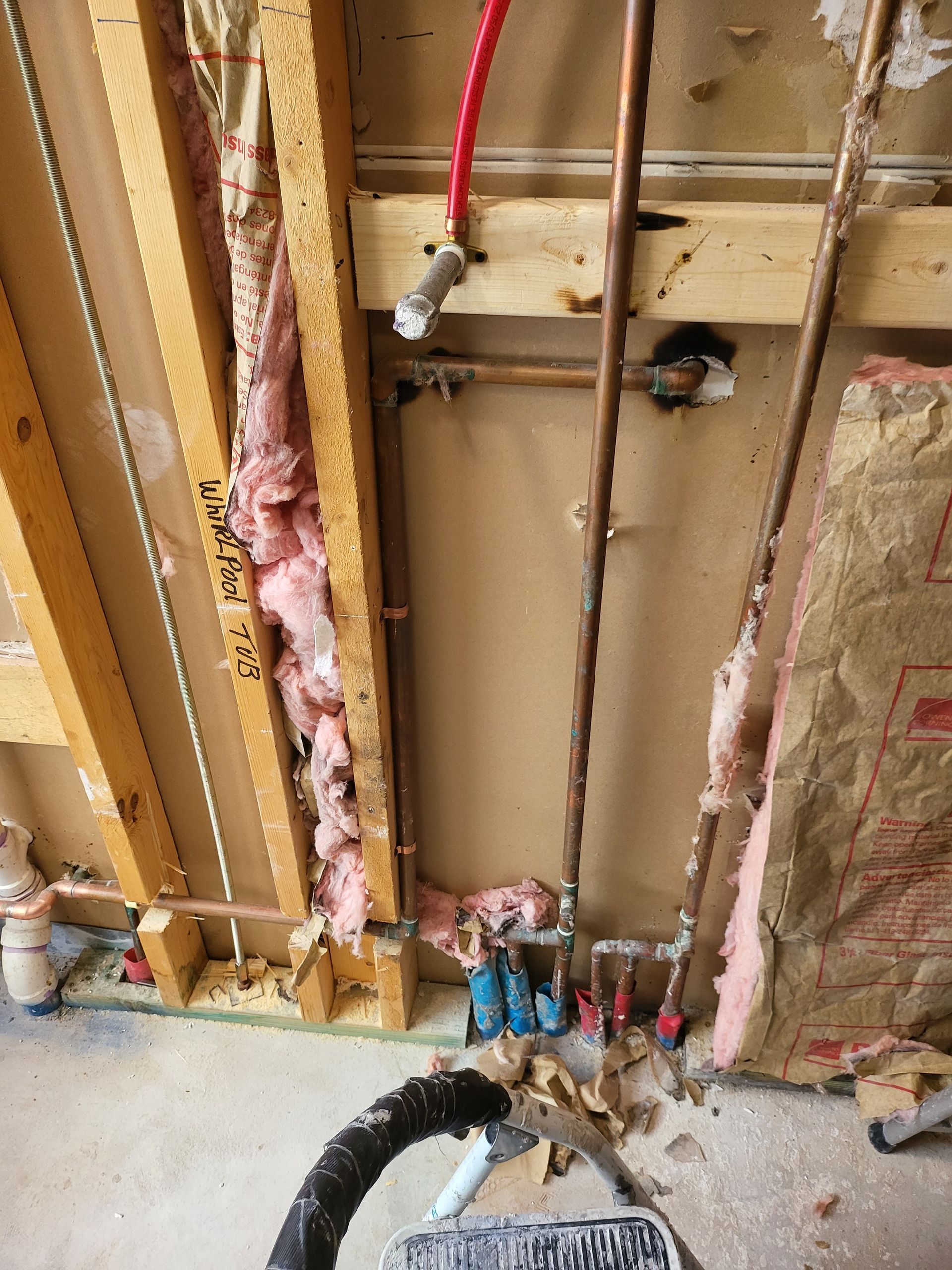 Exposed wall framing with plumbing pipes, pink insulation, and electrical wiring under construction