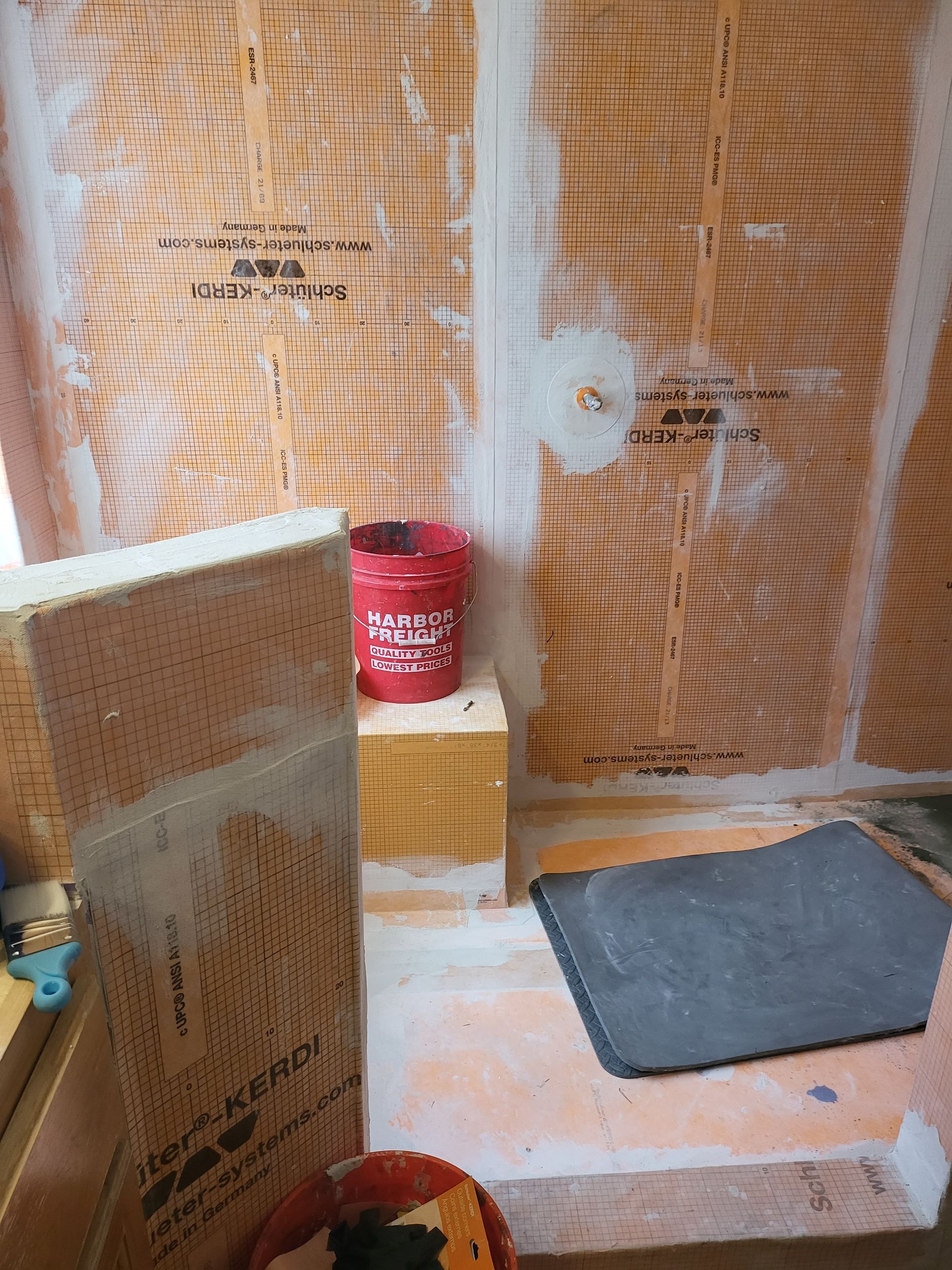 Plastic-covered construction area with a red paint can, wooden boards, and a gray mat on the floor.