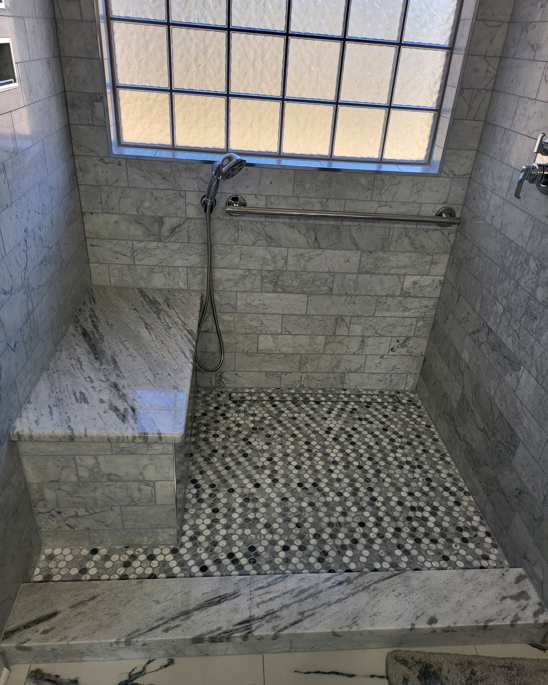 Small unfinished tiled bathroom with shower area, window, and exposed wall plumbing.
