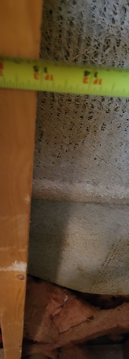 Close-up of a green measuring tape against a textured wall and exposed brown wood.