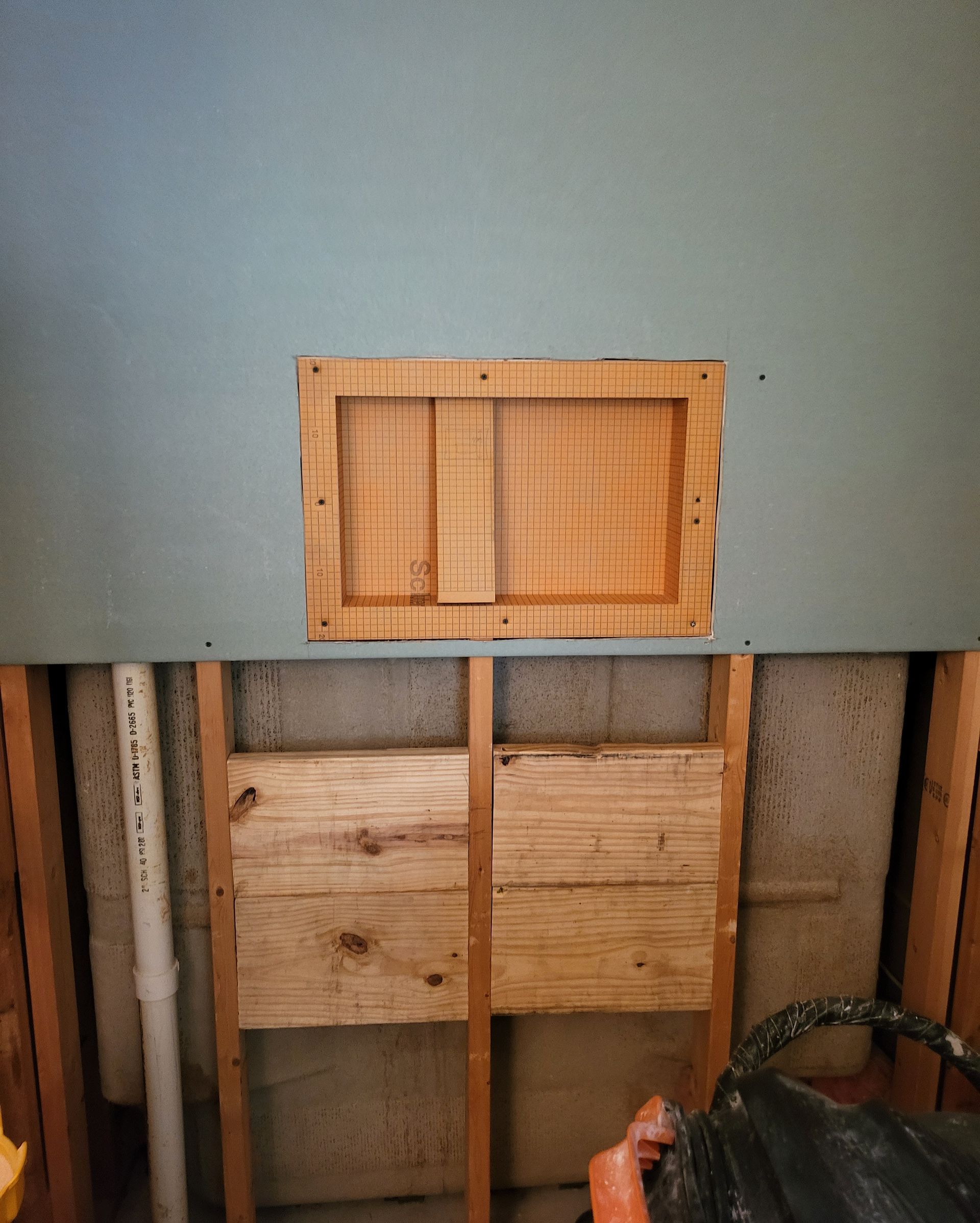 Partially finished wall with exposed studs and a small wood-framed opening, seen from inside a room