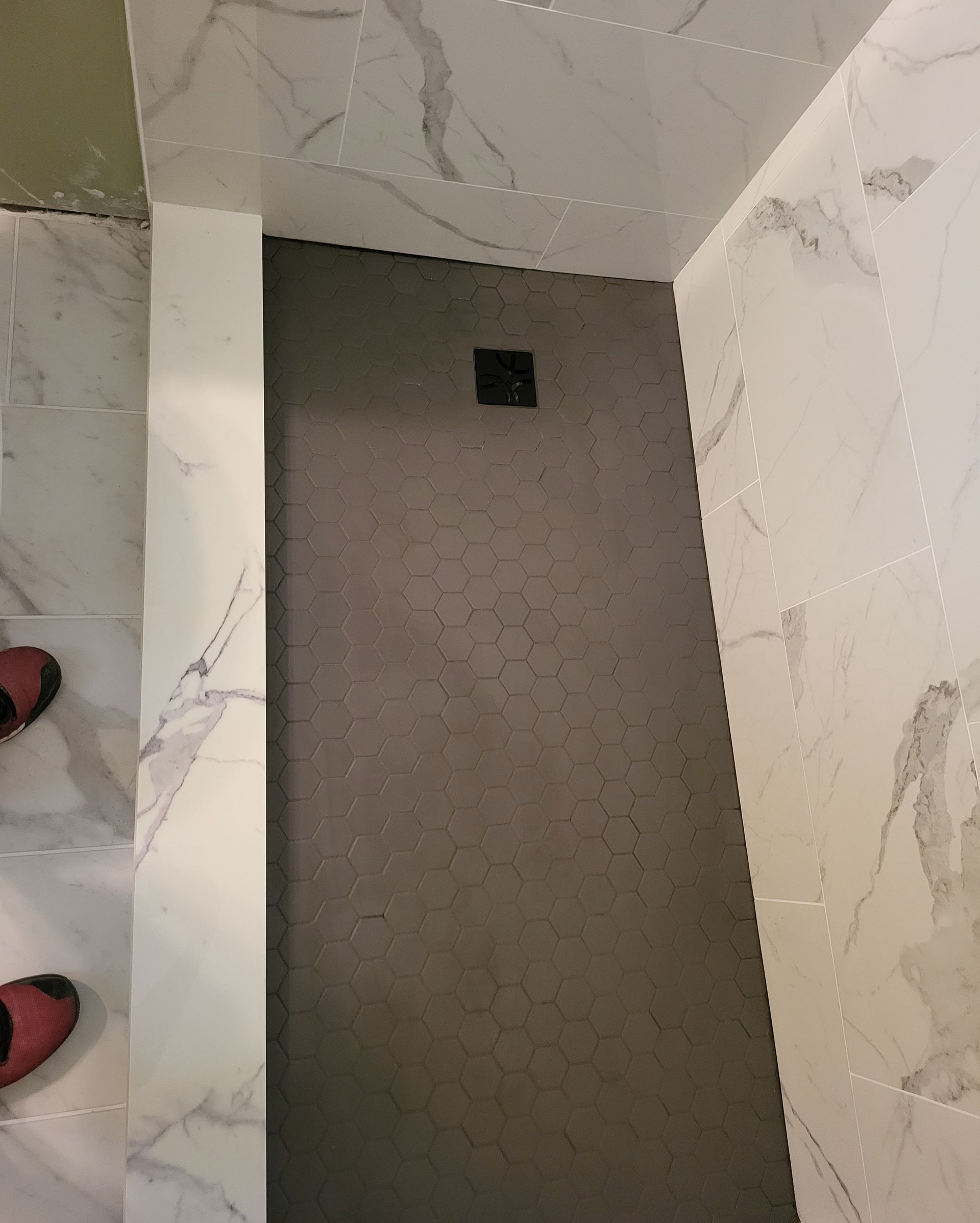 A narrow carpeted alcove with a small square floor drain between white marble walls.