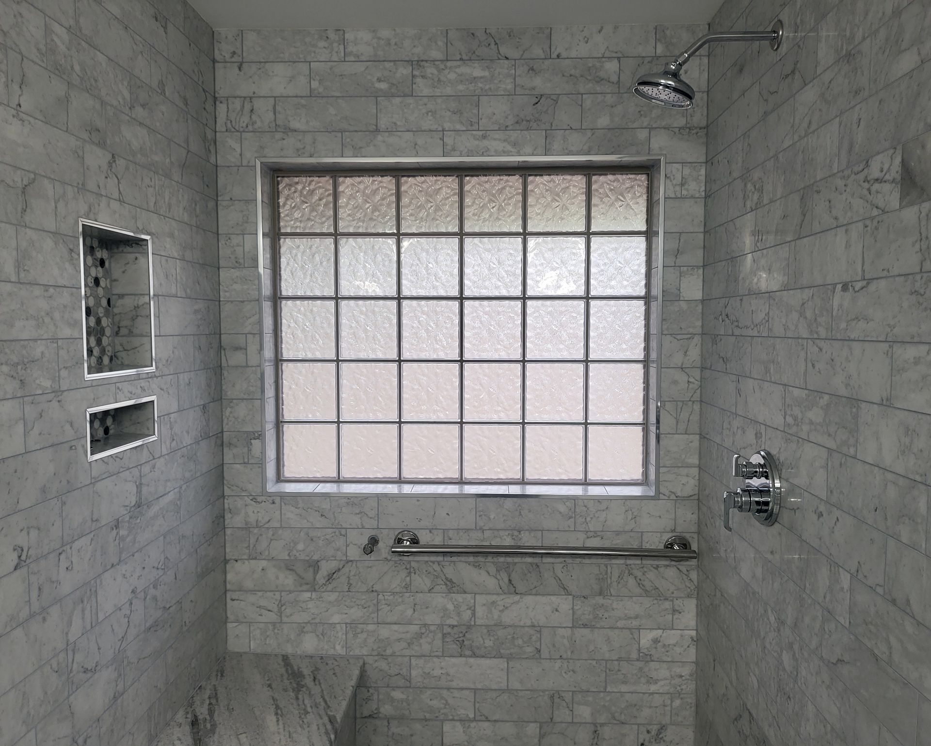 Tiled shower stall with window, built-in shelf, and chrome shower fixtures