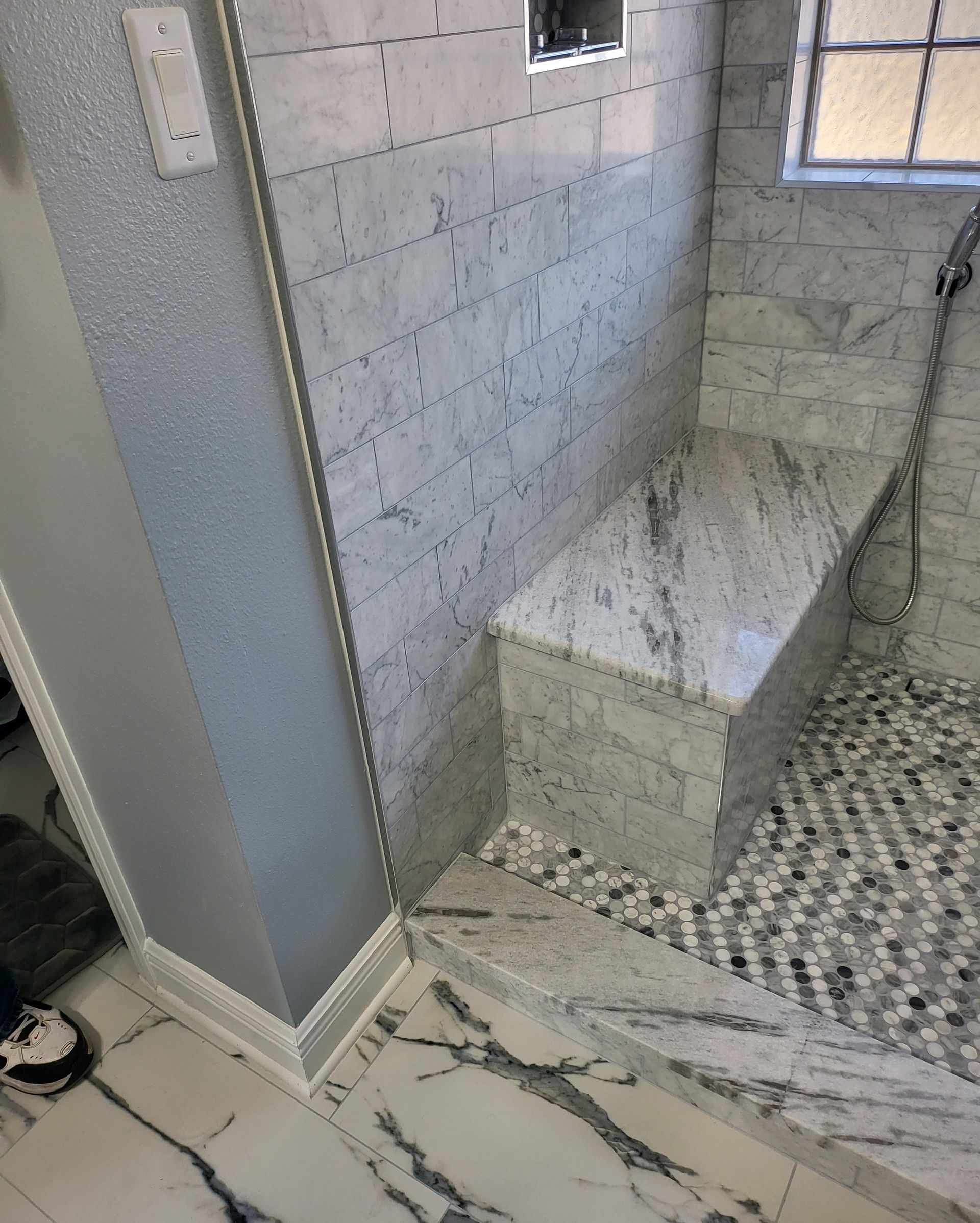 Bathroom shower with marble-pattern tile, built-in bench, and pebble mosaic floor
