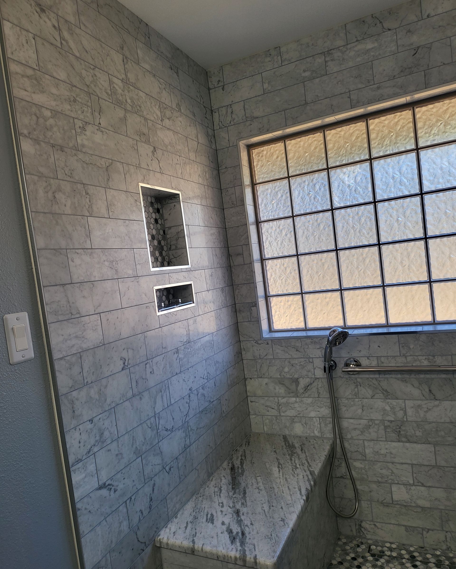Small tiled bathroom with shower and frosted window, lit by daylight