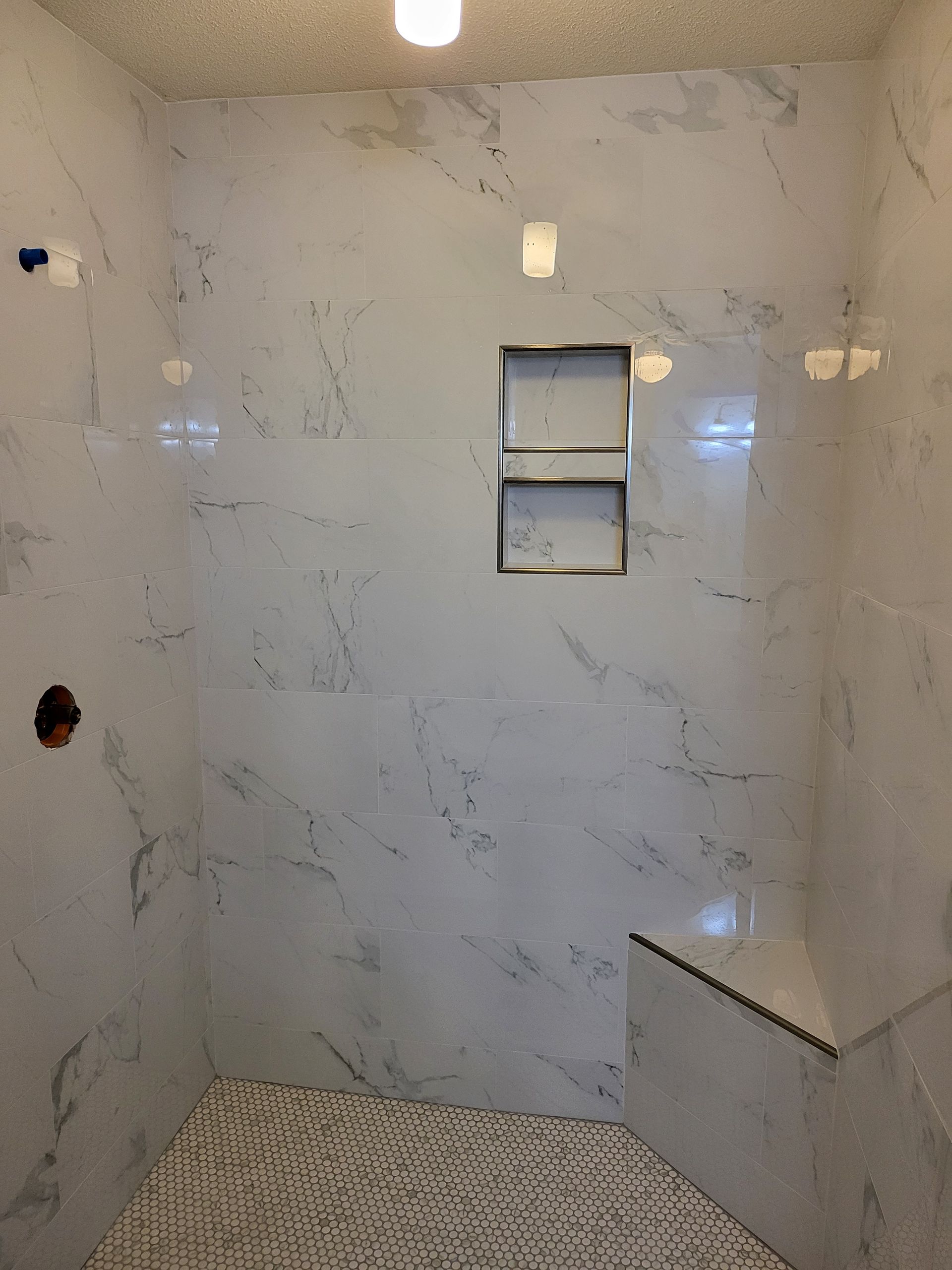 Modern shower stall with marble-look tile, built-in shelves, and pebble mosaic floor。