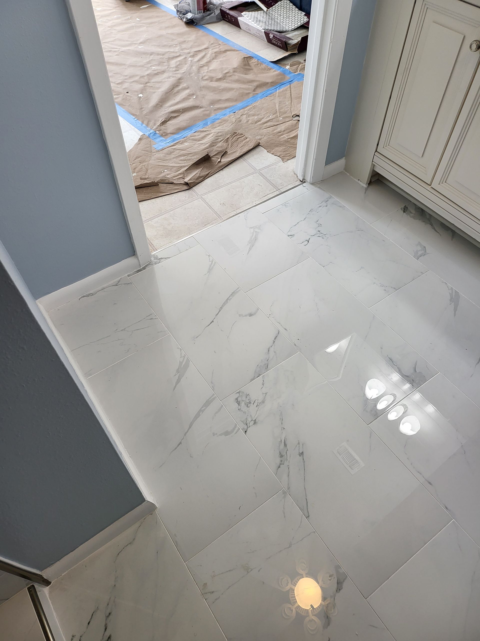 White tiled floor at a doorway with a rug and blue painter’s tape leading into another room