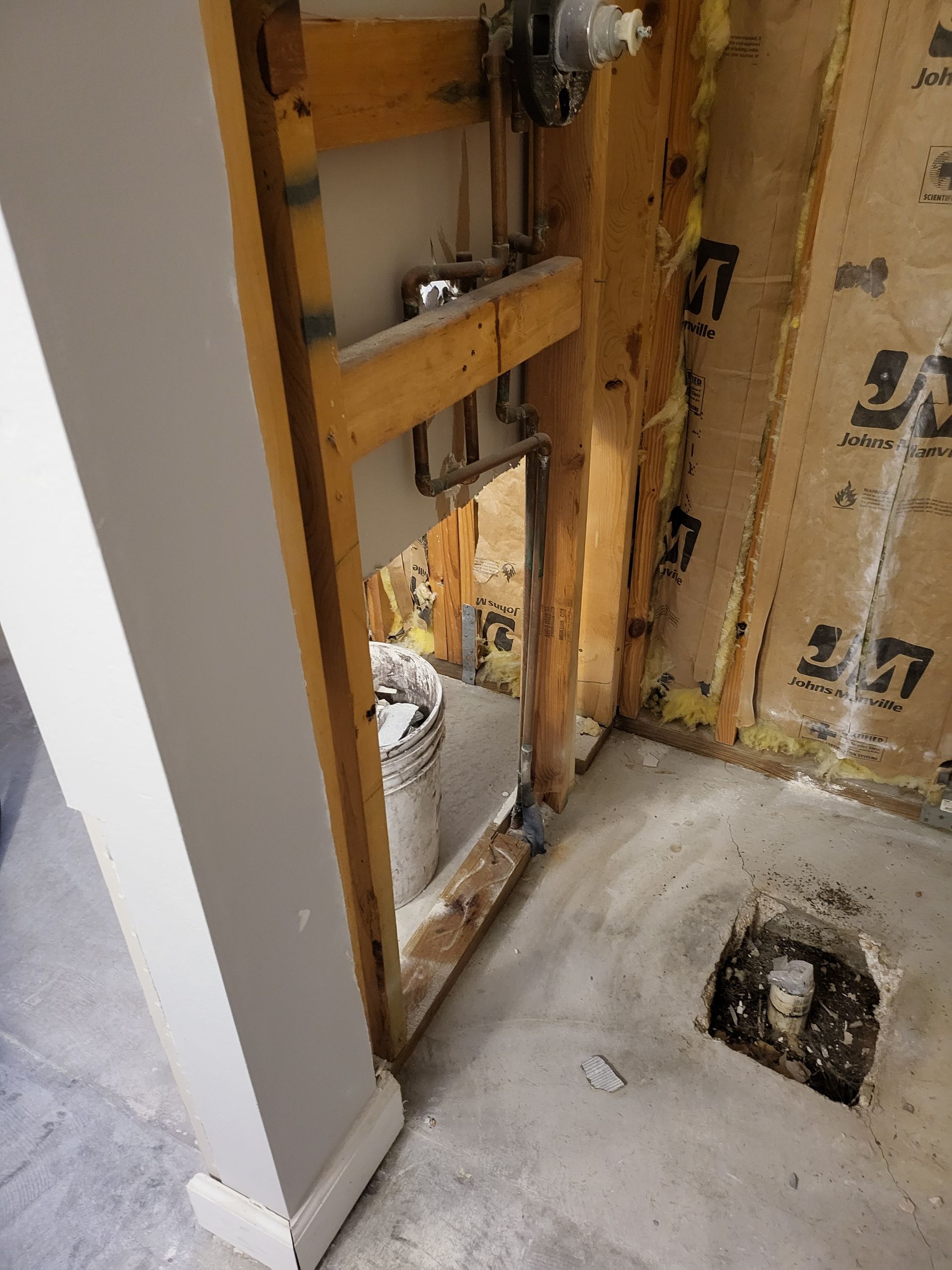 Partially demolished interior wall with exposed studs, insulation, and a hole in the concrete floor.
