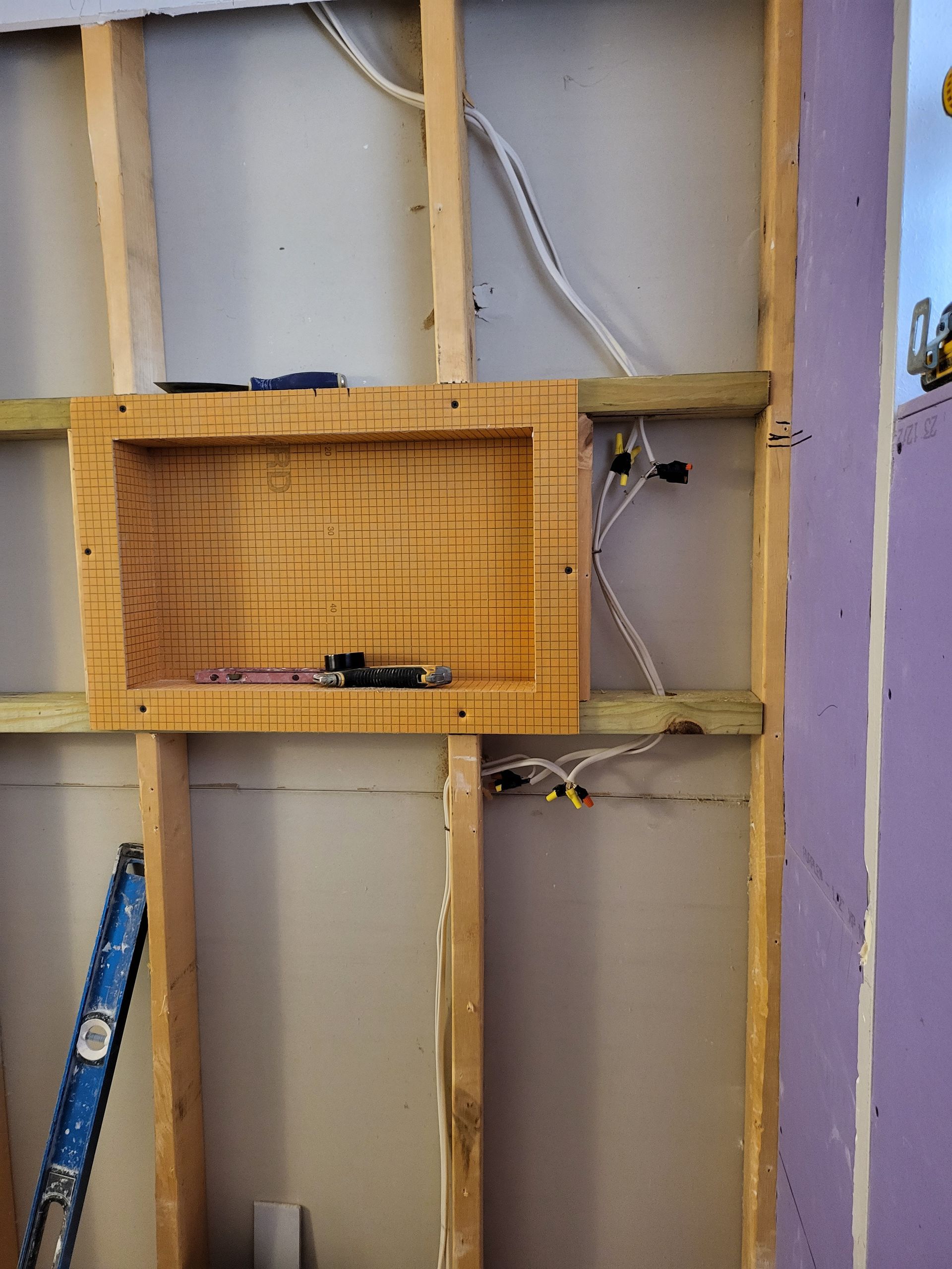 Exposed wall framing with wooden shelf, loose wires, and a small blue ladder in a room under renovation