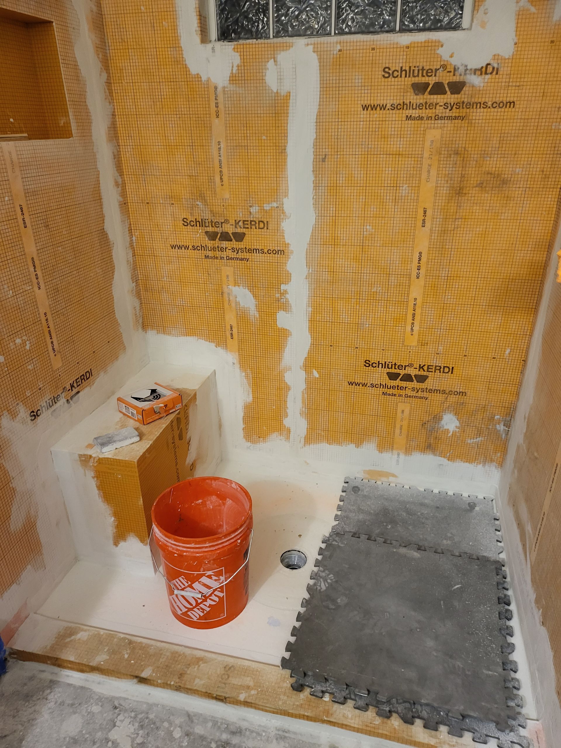 Interior wall under renovation with insulation, wallboard, red bucket, and floor mat.