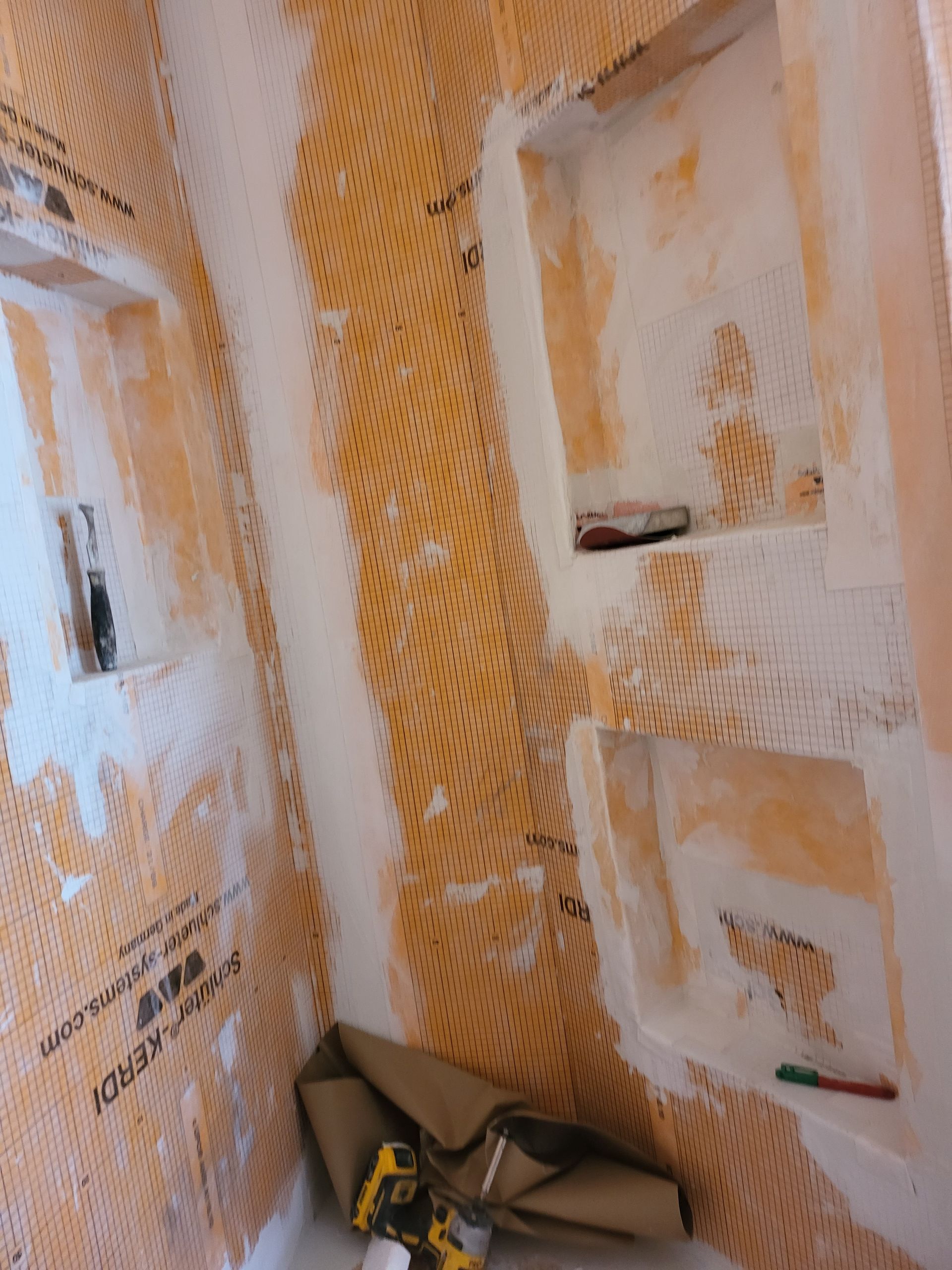 Peeling orange paint and white textured walls in a narrow interior corner with masking materials near the floor