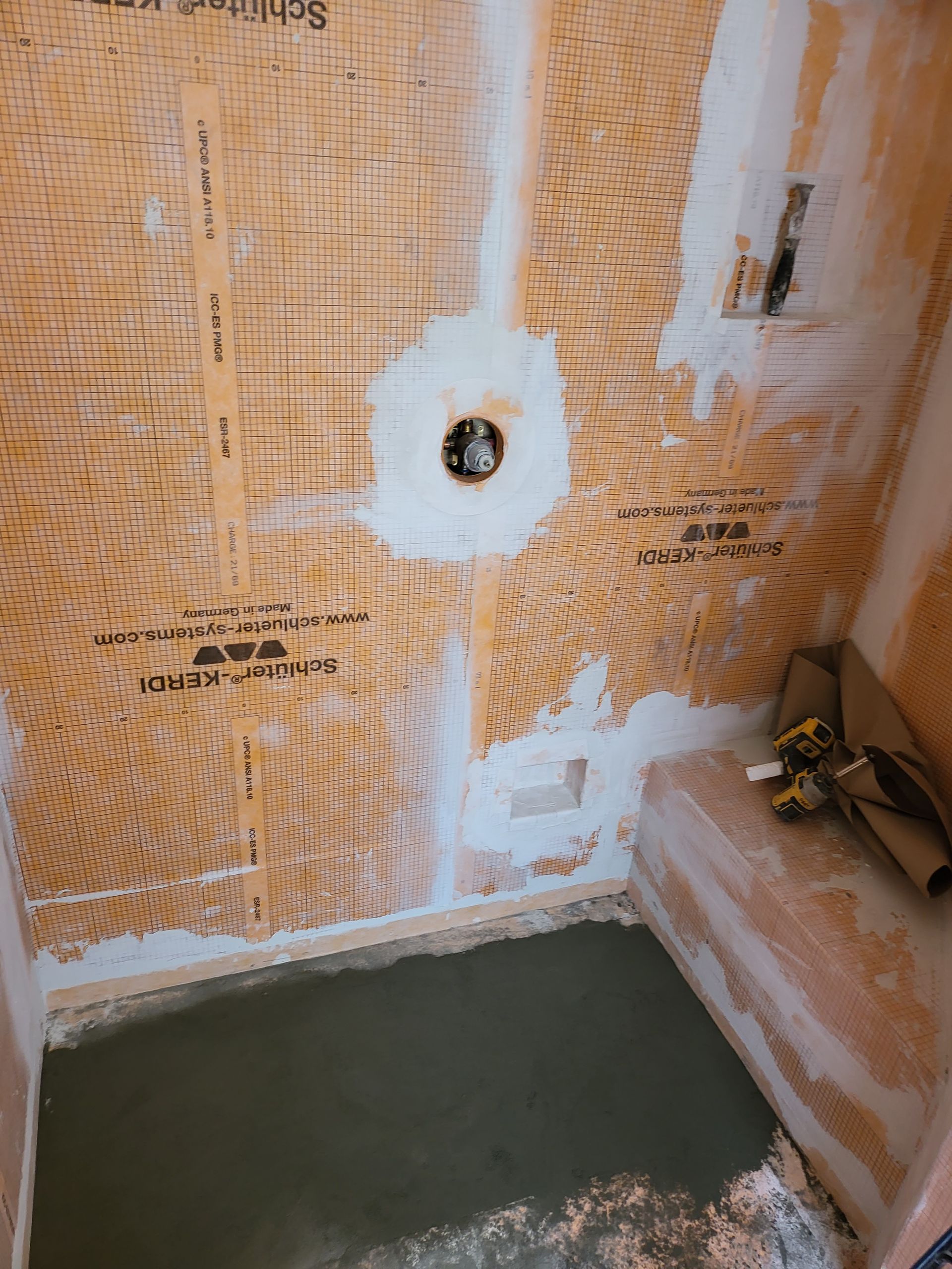 Bathroom wall with stripped wallpaper, a hole for plumbing, and a green floor basin area