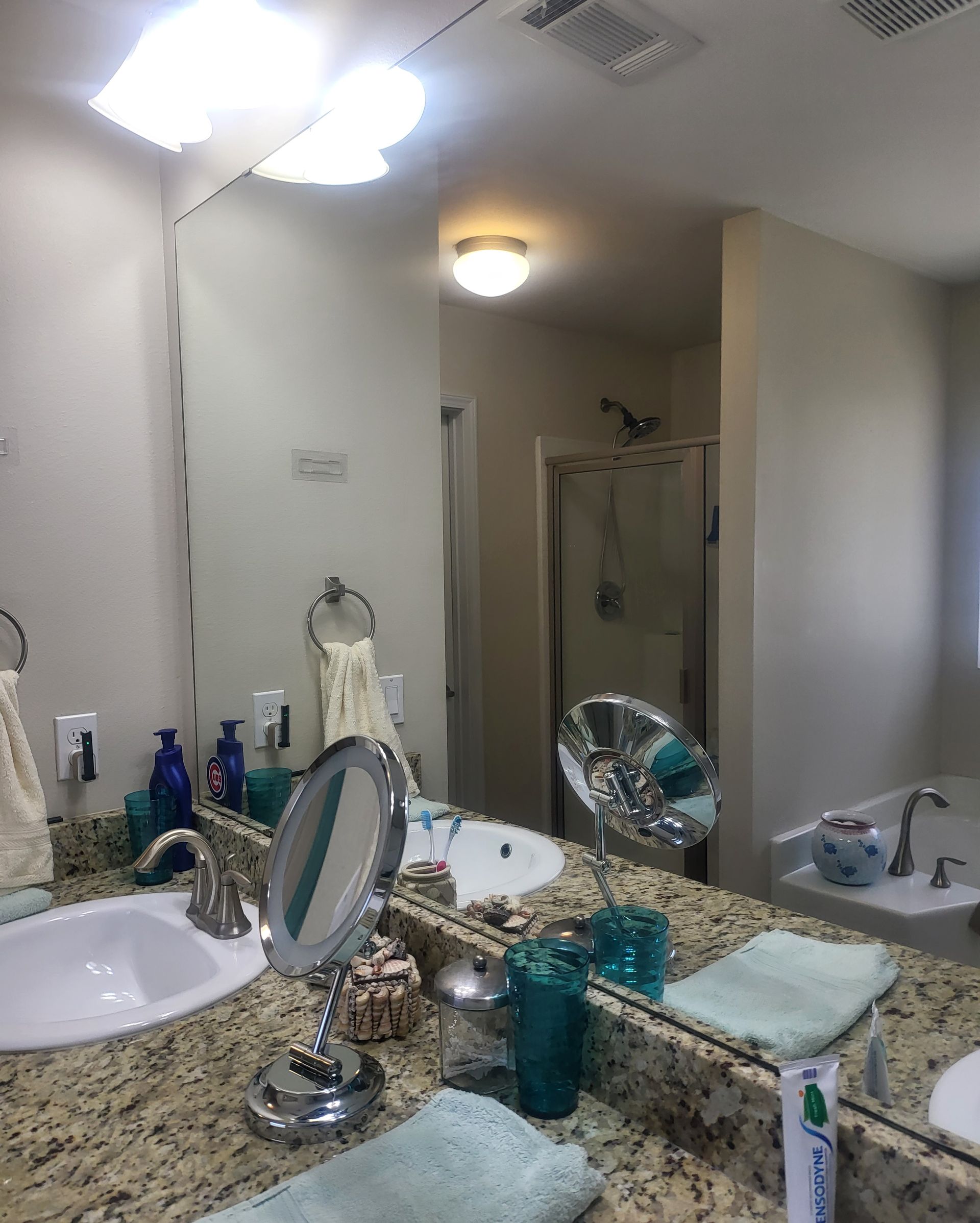 Bathroom vanity with sink, mirror, toiletries, and a shower in the background.