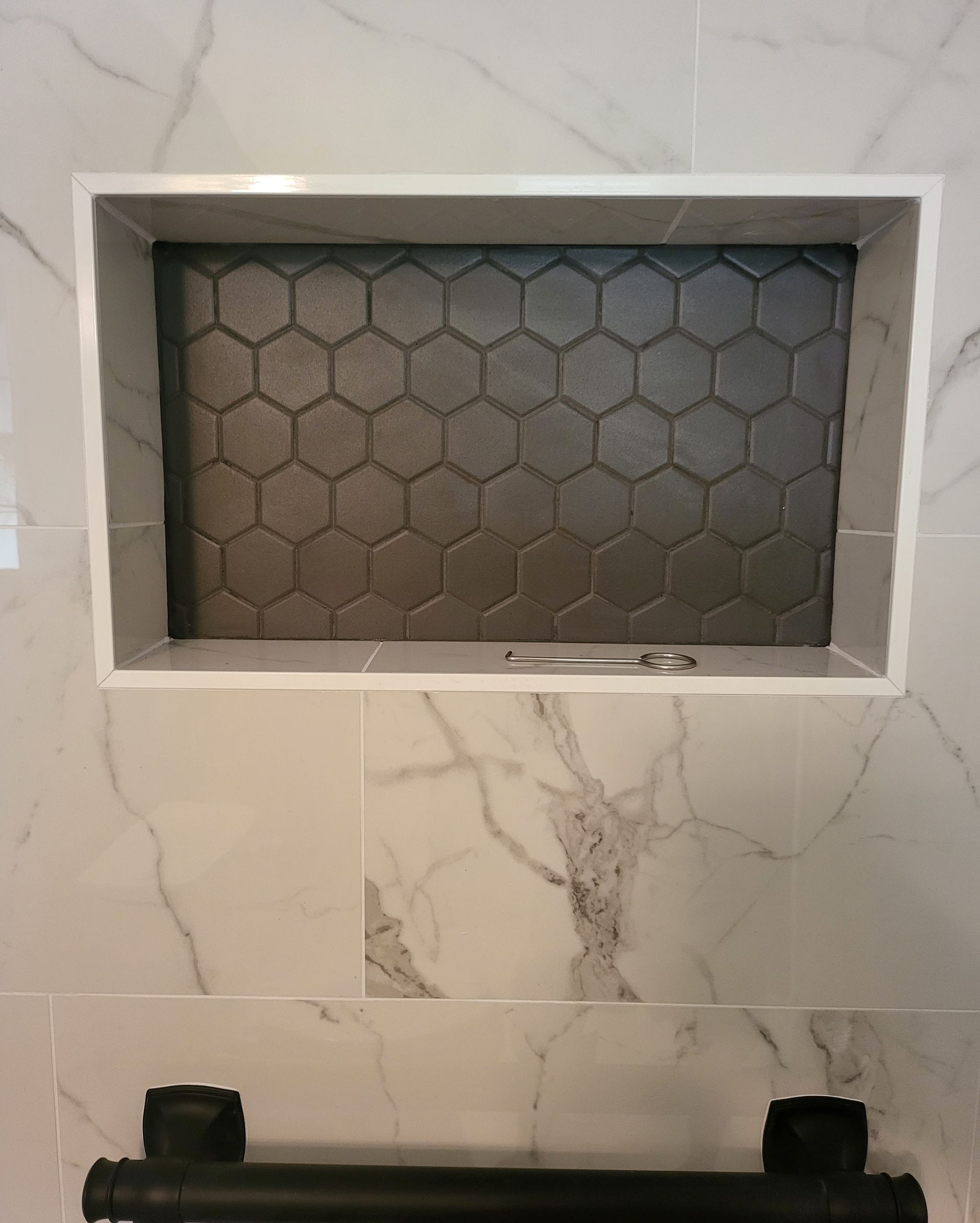 Built-in shower niche with hexagonal dark tile inset in a light marble-pattern wall.