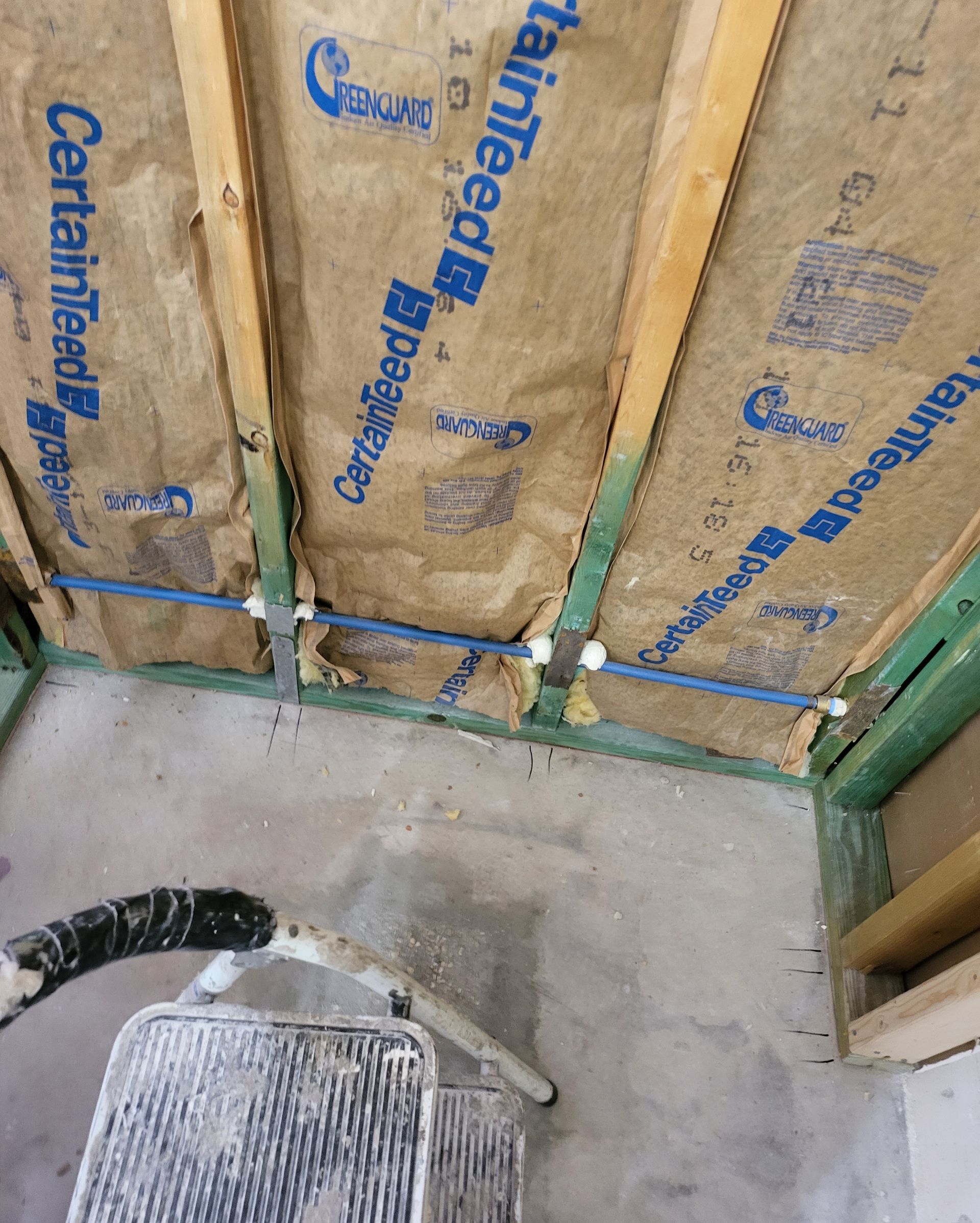 Insulated wall framing with blue-backed panels and a concrete floor in an unfinished room.