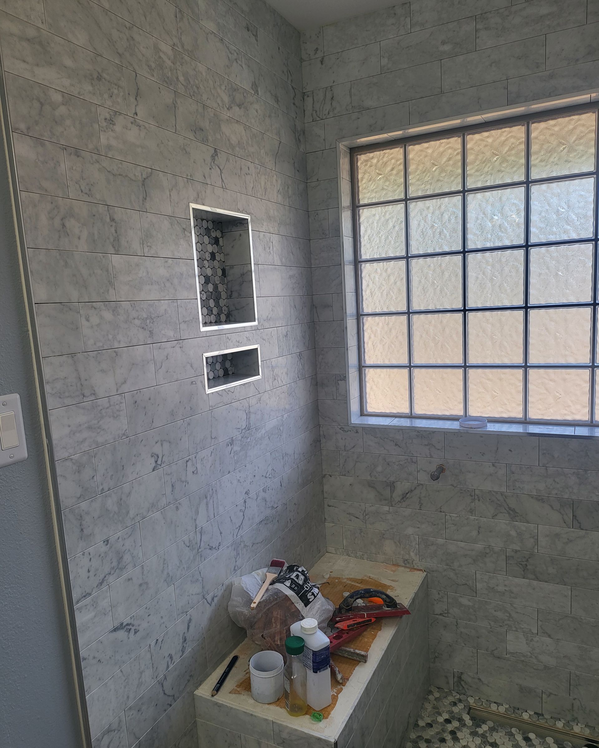 Unfinished gray cinder-block room with a window, two wall openings, and construction supplies on a tray.