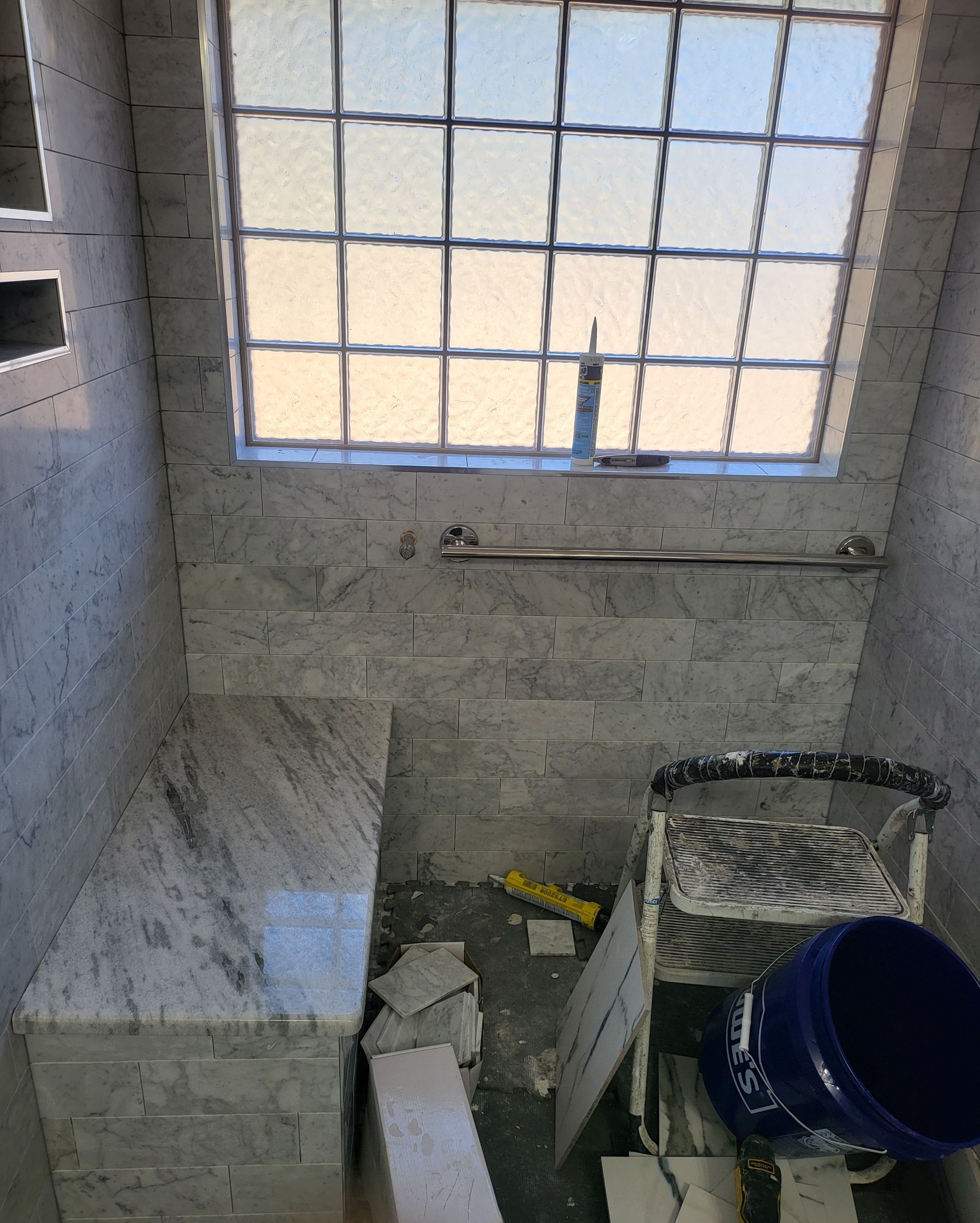 Small tiled bathroom under construction with a window and buckets on the floor.