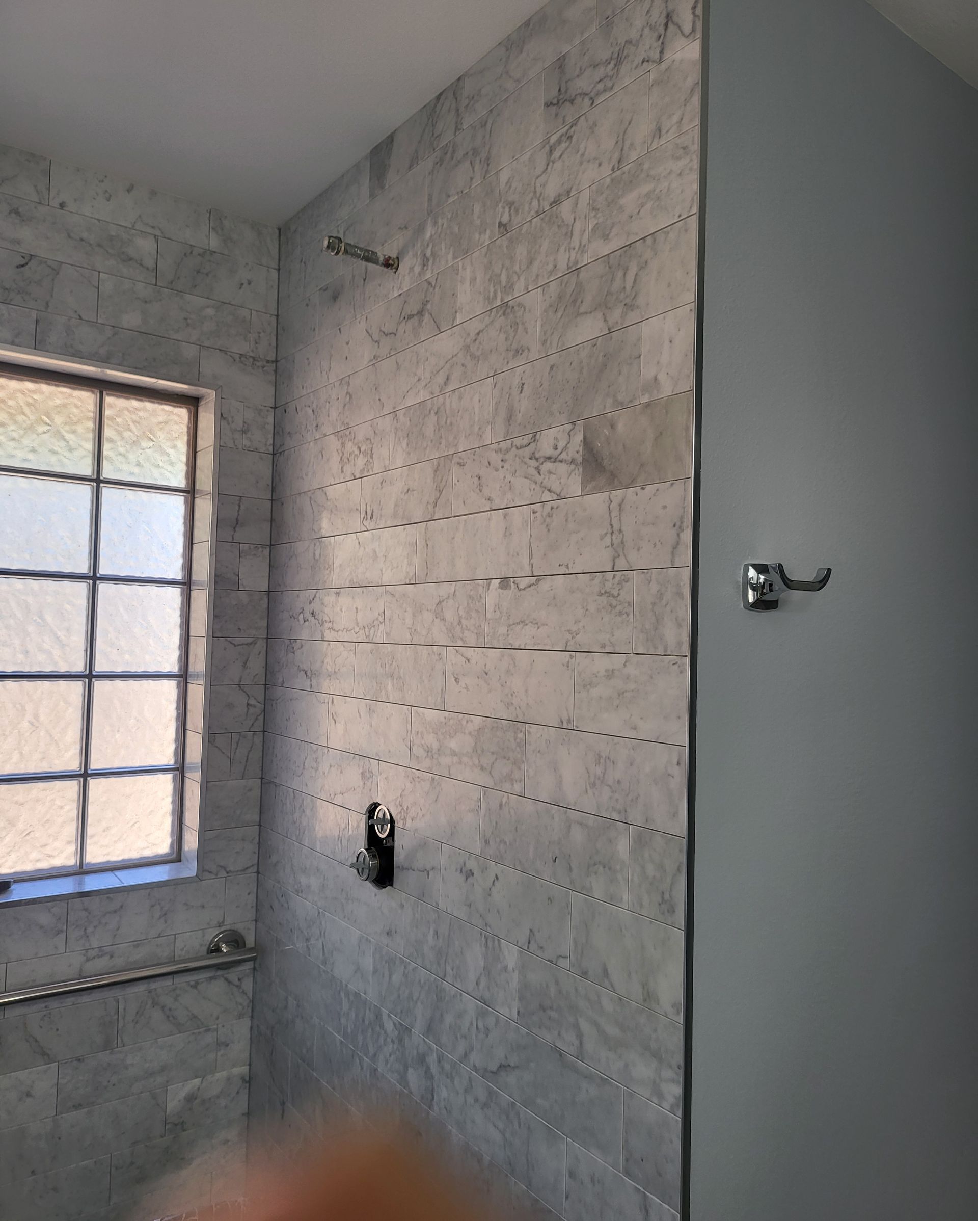 Unfinished bathroom with gray cinder block walls, small window, and shower fixtures.