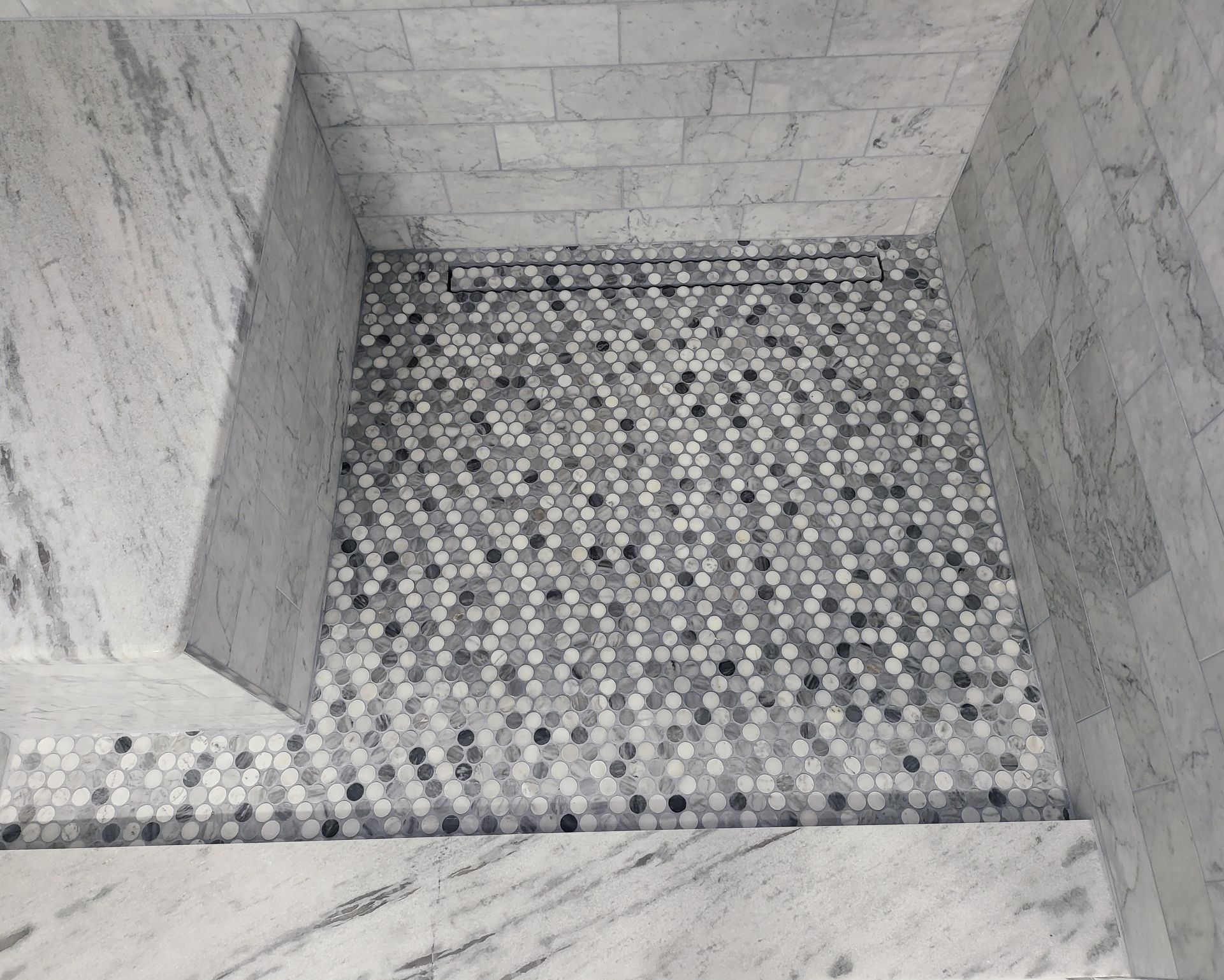 Small tiled shower stall with gray marble walls and a black-and-white mosaic floor.