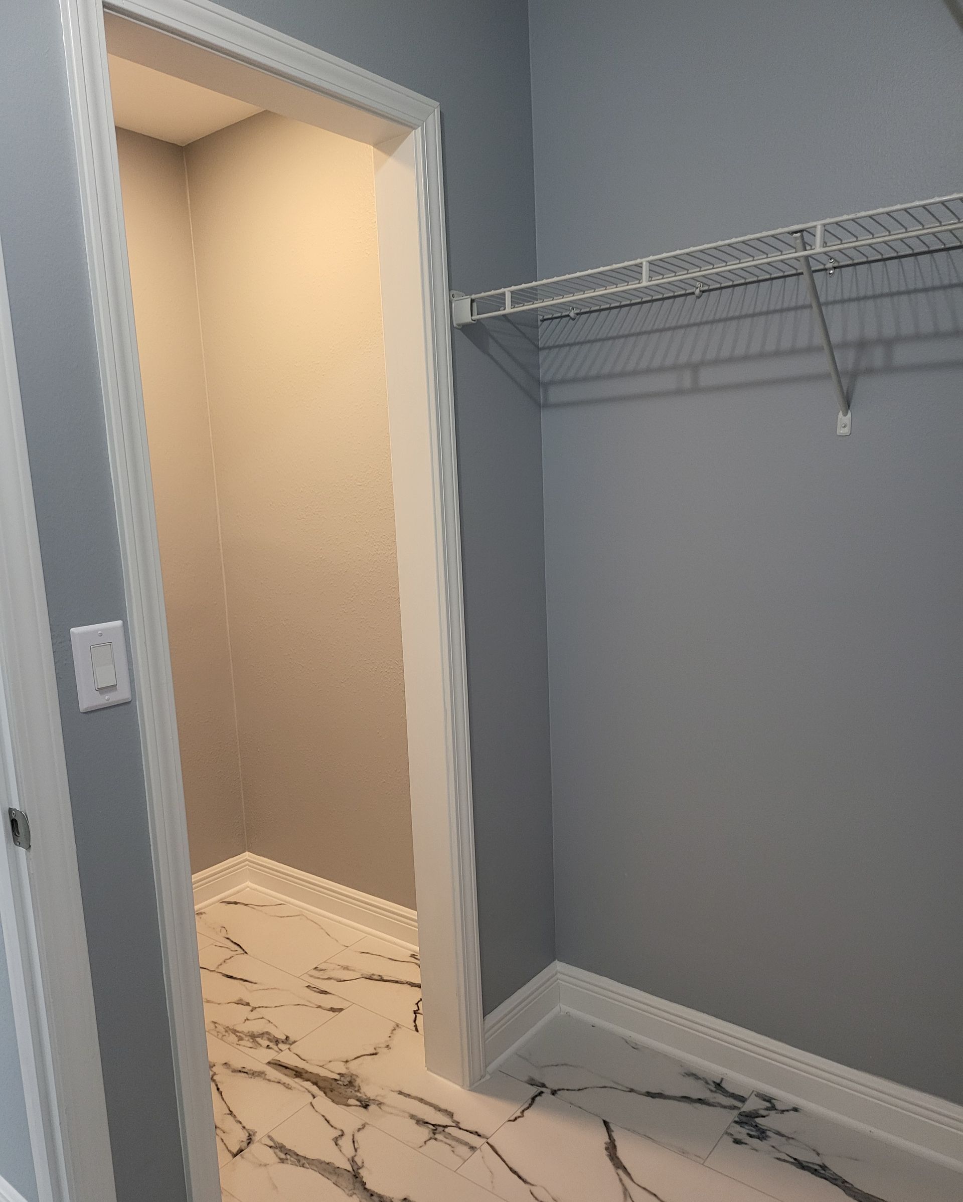 Empty closet with gray walls, white wire shelving, and an open doorway to a lit adjacent room.
