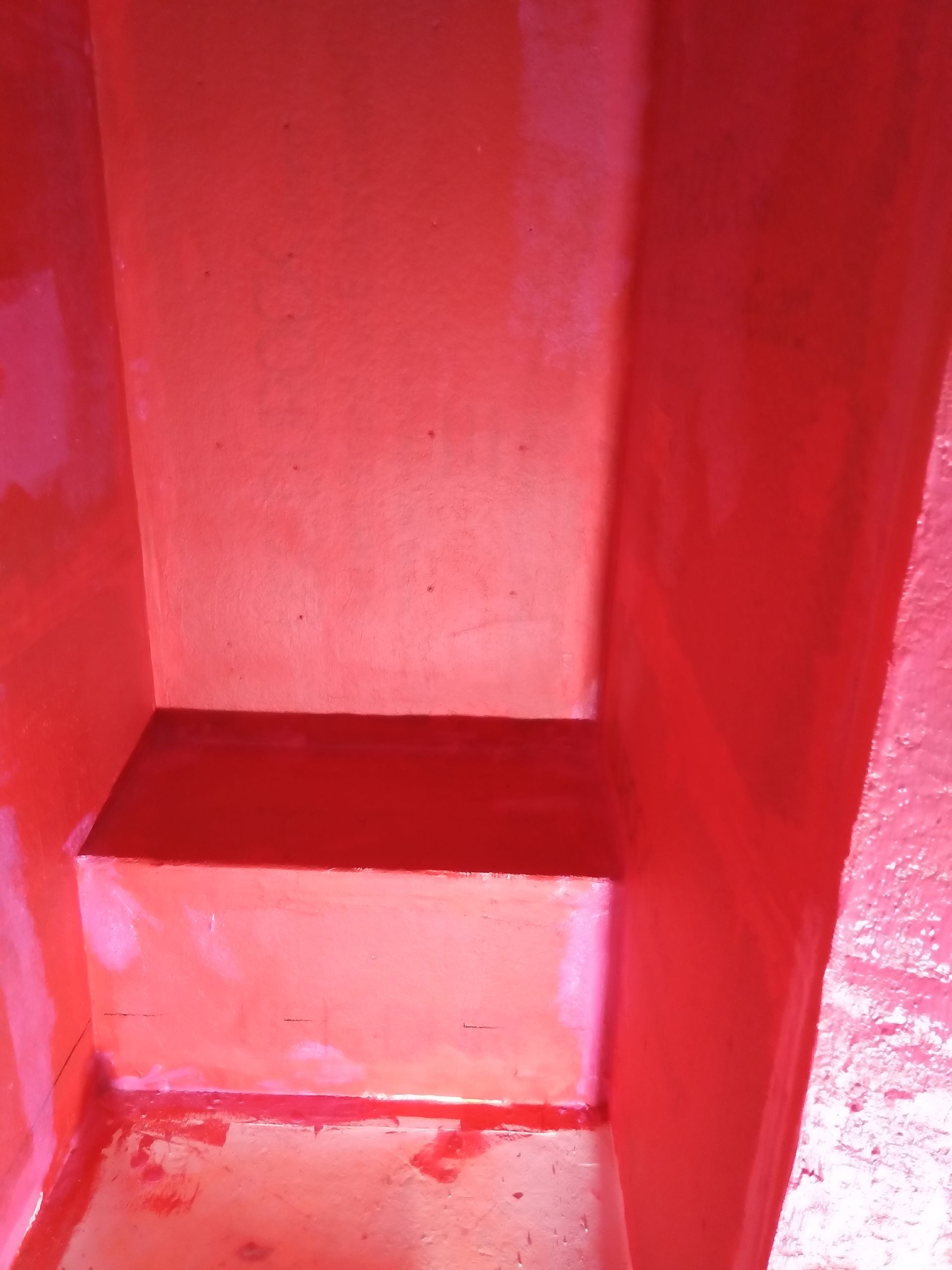Red-lit empty stairwell with a small concrete step and walls, viewed from below