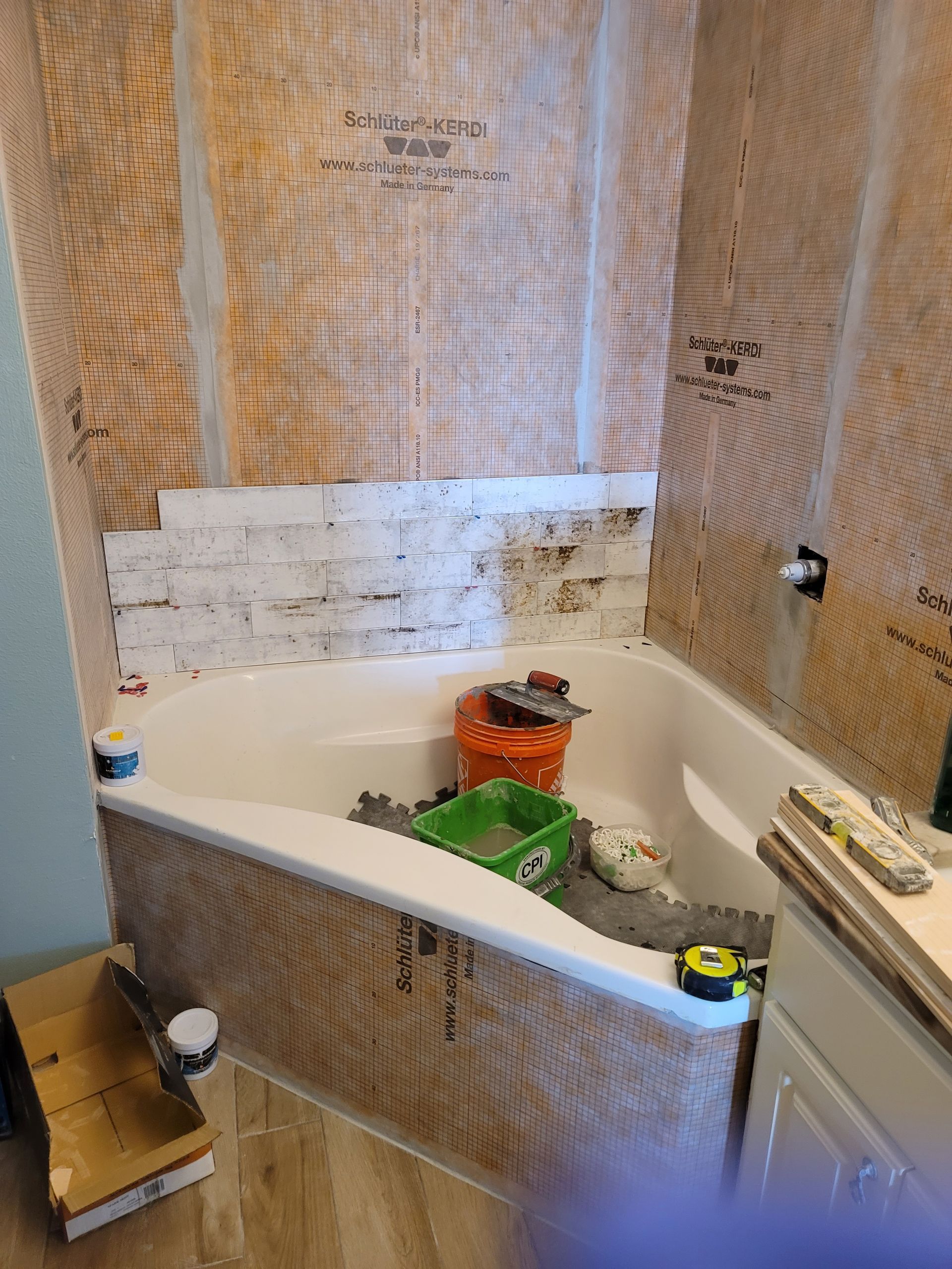 Bathroom with a bathtub and shower walls, cluttered with tools and supplies during renovation.