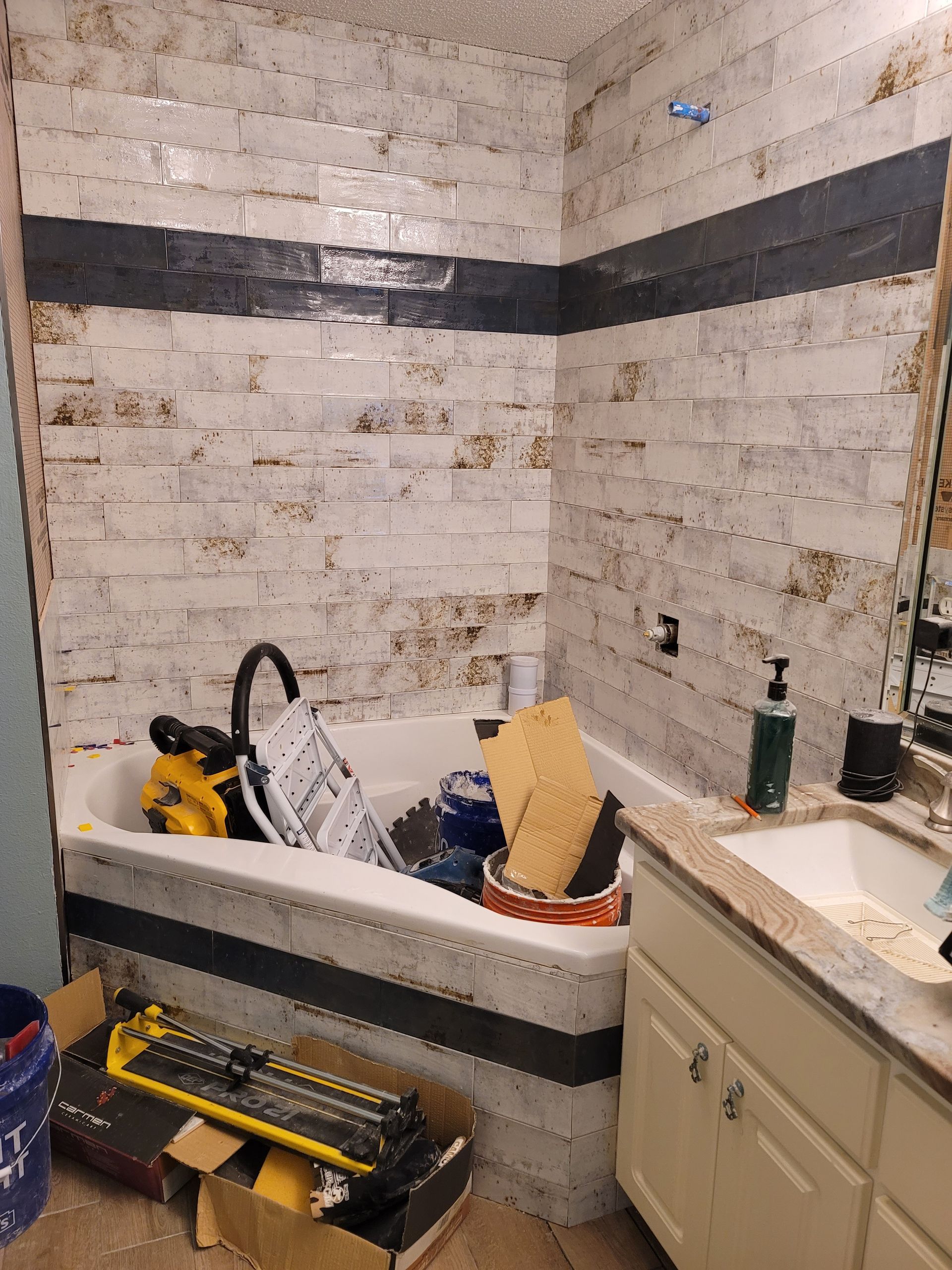 Small bathroom under renovation with exposed white brick, bathtub, sink, tools, and construction debris.