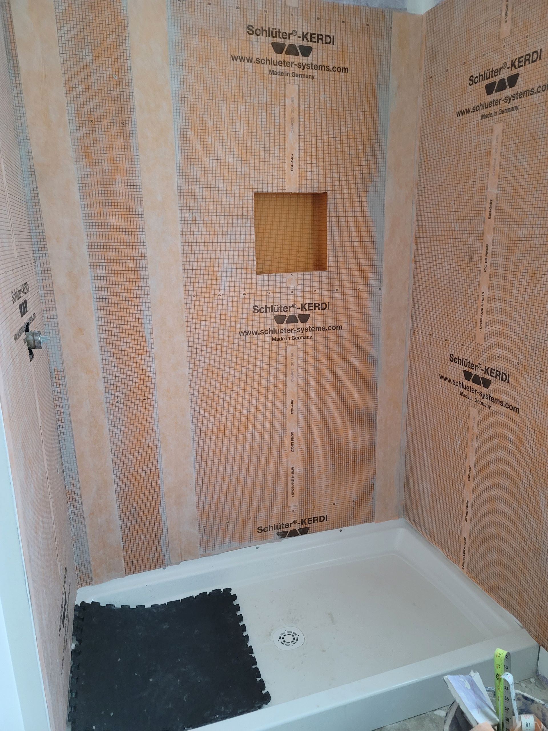 Bathroom shower under construction with wood framing, wall markings, and a white shower pan.