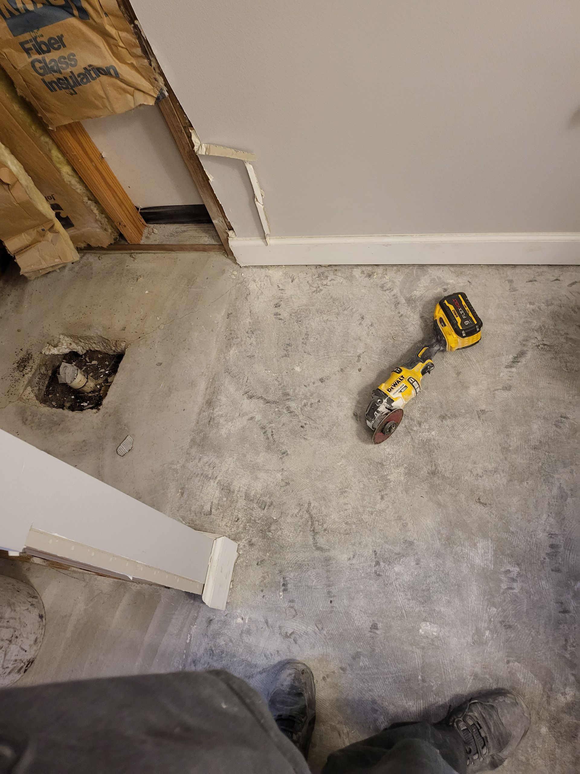 Construction debris-covered floor with a yellow cordless drill near a wall opening and exposed studs.