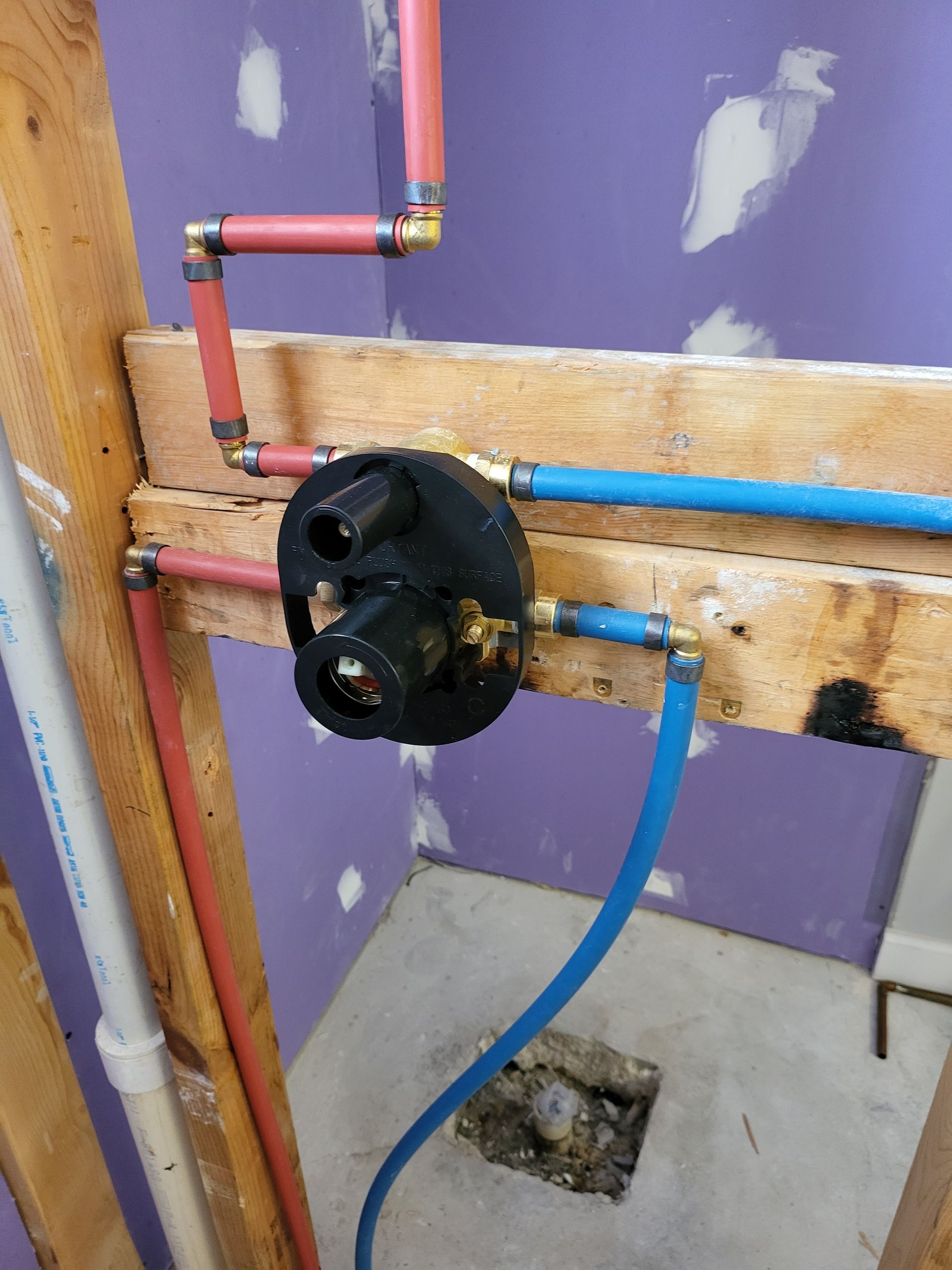 Plumbing pipes and a black valve assembly mounted on a wooden board against a purple wall.