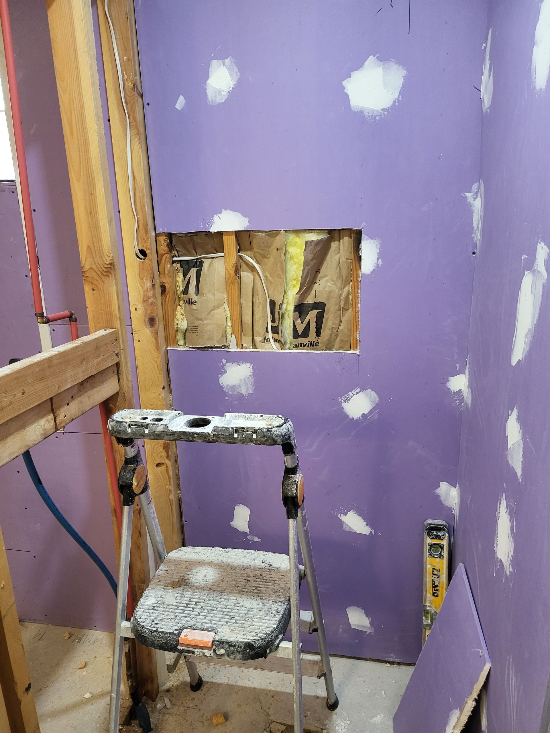 Small bathroom under renovation with purple drywall, exposed studs, a step ladder, and wall opening.