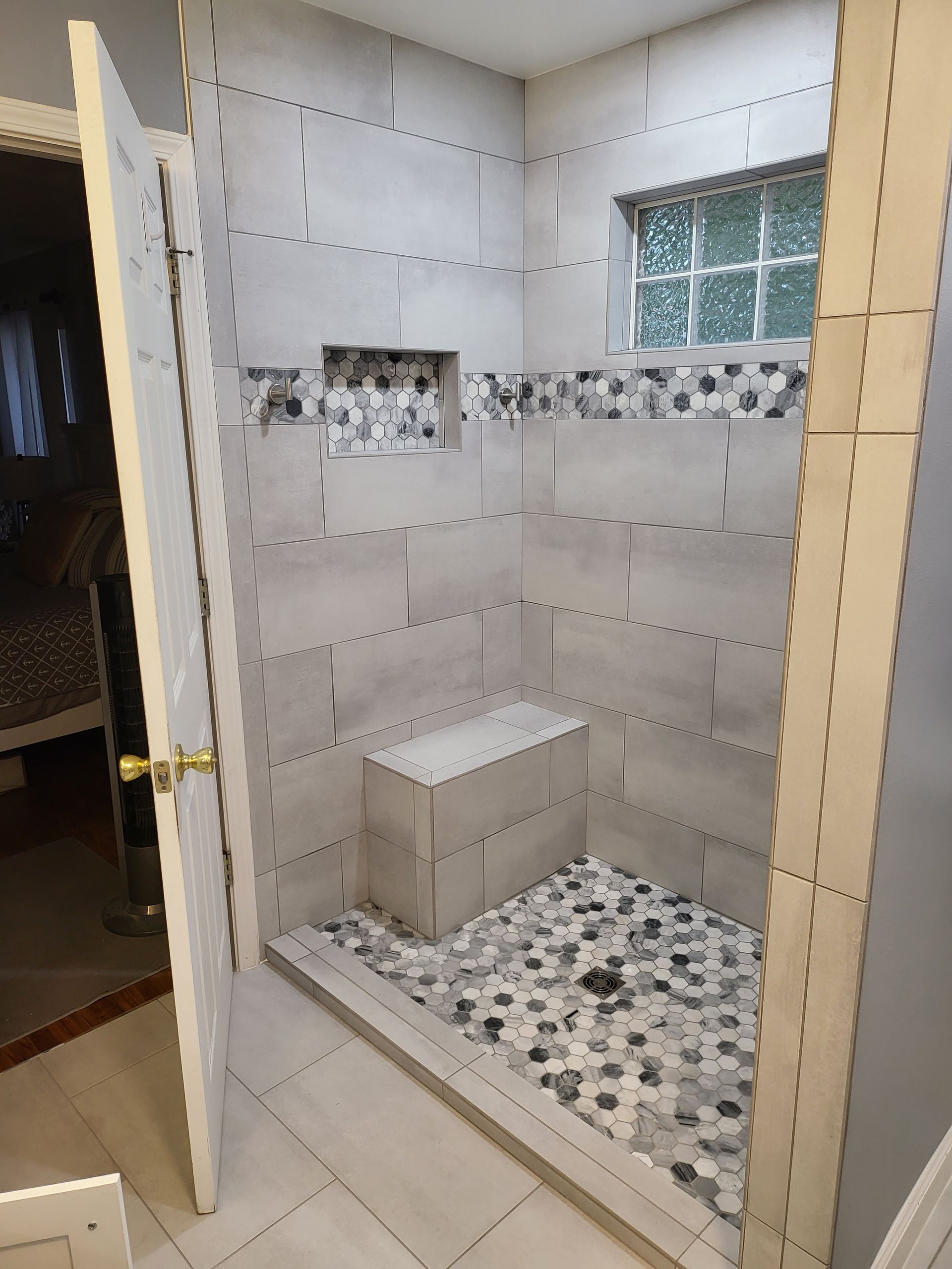 Tiled shower stall with a bench, pebble shower floor, decorative accent strip, and small window.