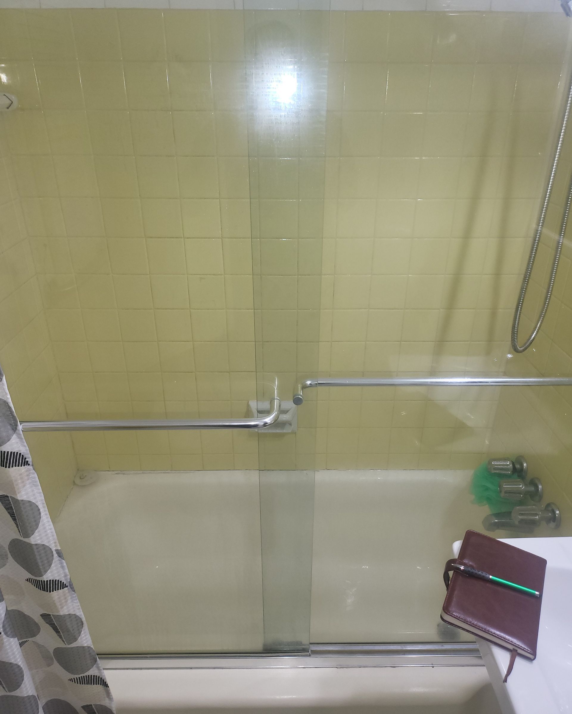 Bathroom with yellow tiled shower wall, glass door, and a small stool in the corner.