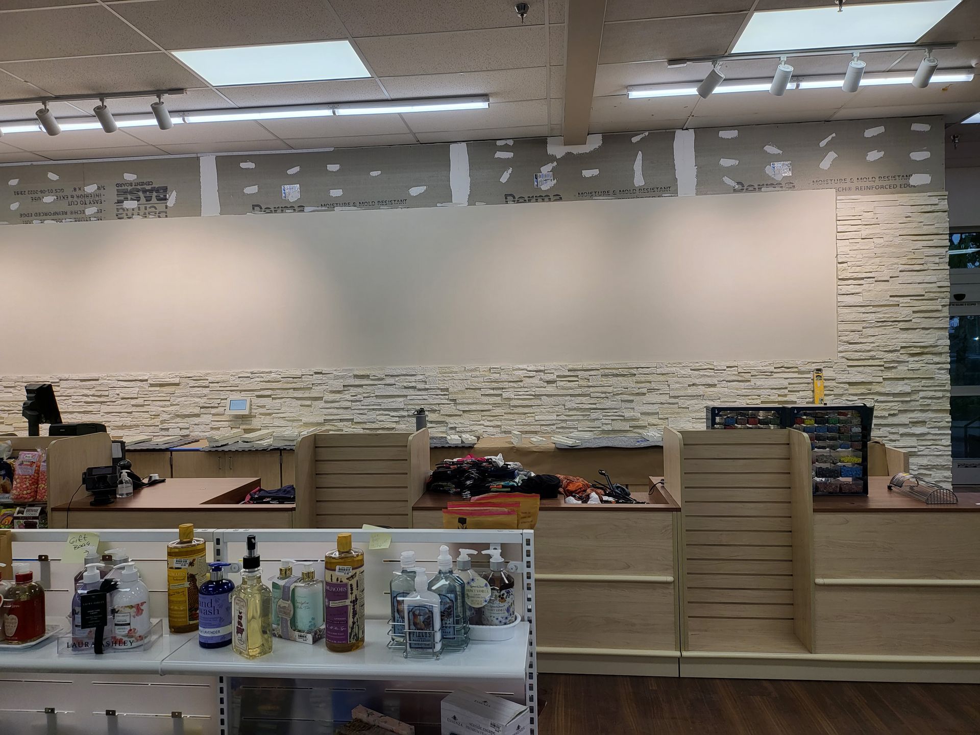 Empty retail counter with shelves of bottled products in the foreground and a stone-textured wall behind.
