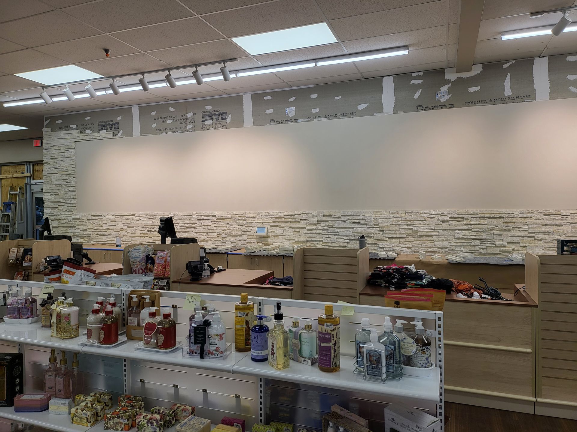 Store checkout area with shelves of candles and jars in the foreground and a blank wall behind.