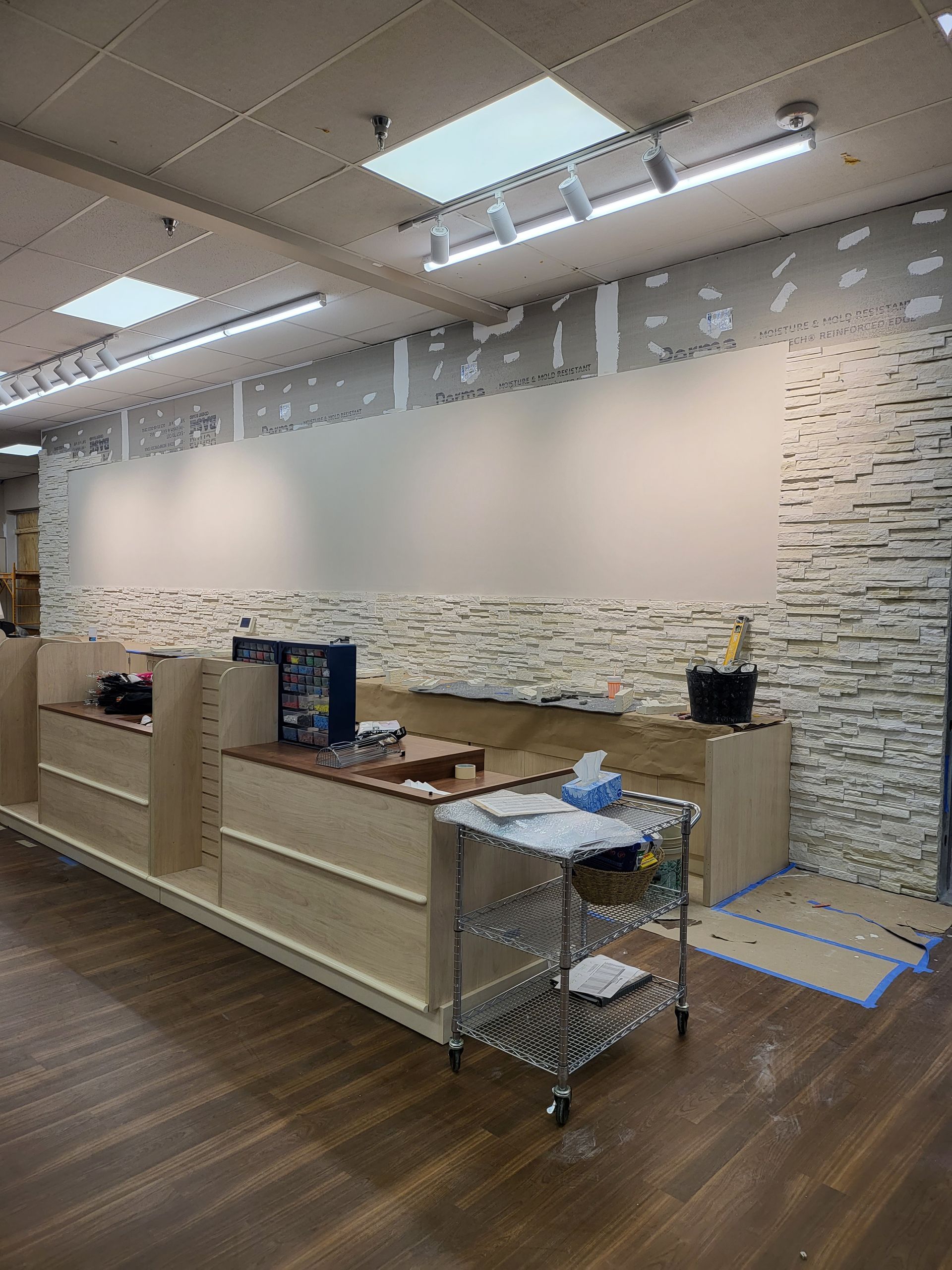 Empty modern office reception area with desks, shelving, white walls, and overhead fluorescent lights