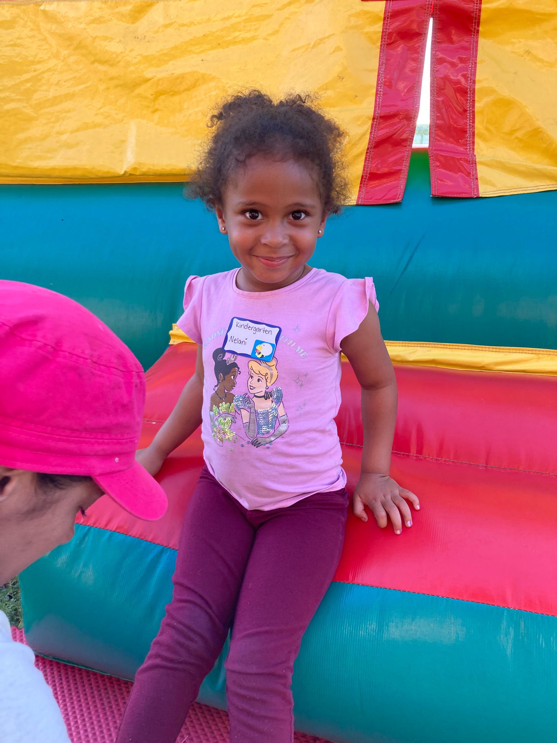 Young child in pink shirt and purple leggings, smiling on a colorful inflatable.