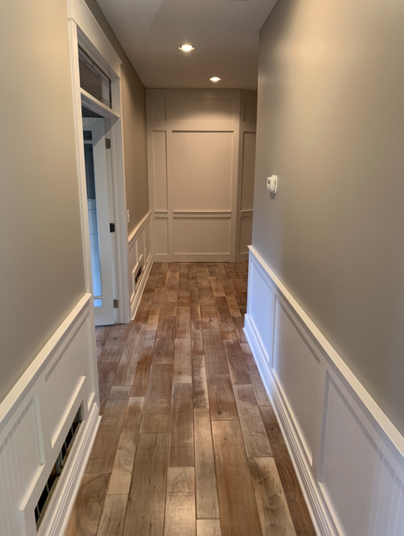 Narrow hallway with wood flooring, white trim, and tan walls.