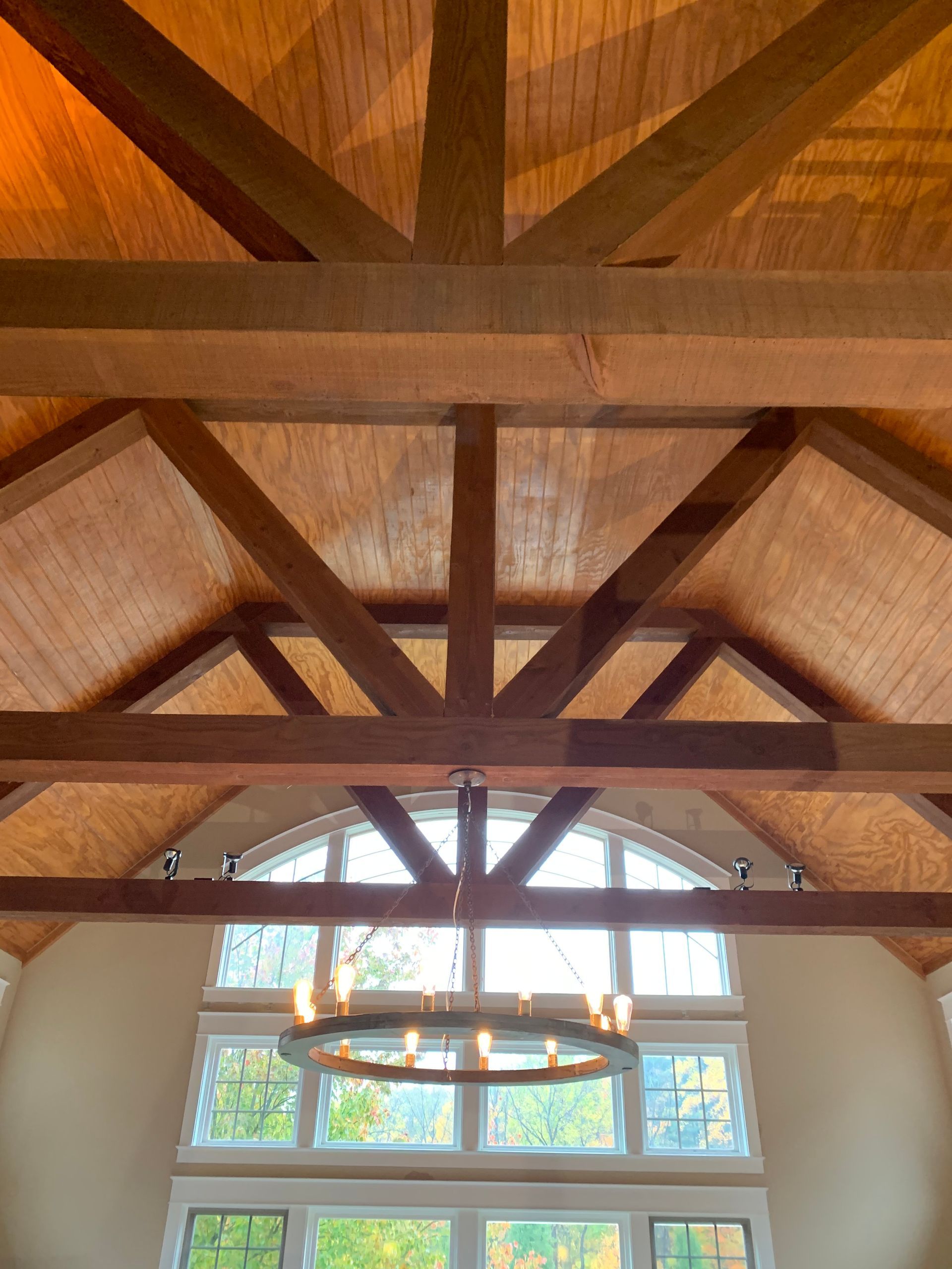 Wooden ceiling with beams and a large, arched window above a chandelier.