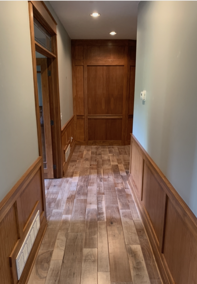 Narrow hallway with wood paneling, light gray walls, and wood-look flooring.