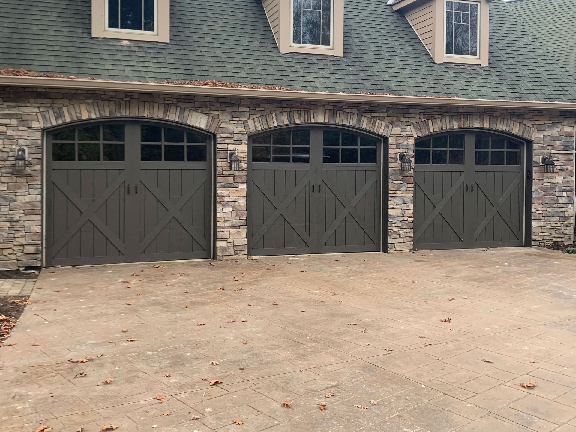 Three gray garage doors with stone accents and a gray shingle roof.
