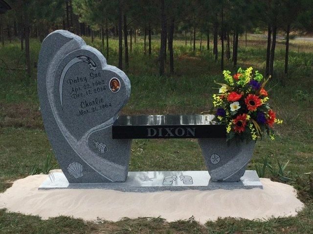 Gray granite tombstone shaped like a heart, with a bench, flowers, and the name