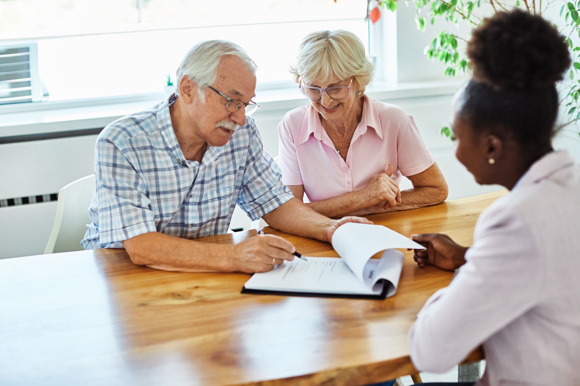 Couple signing documents with an advisor at a wooden table.