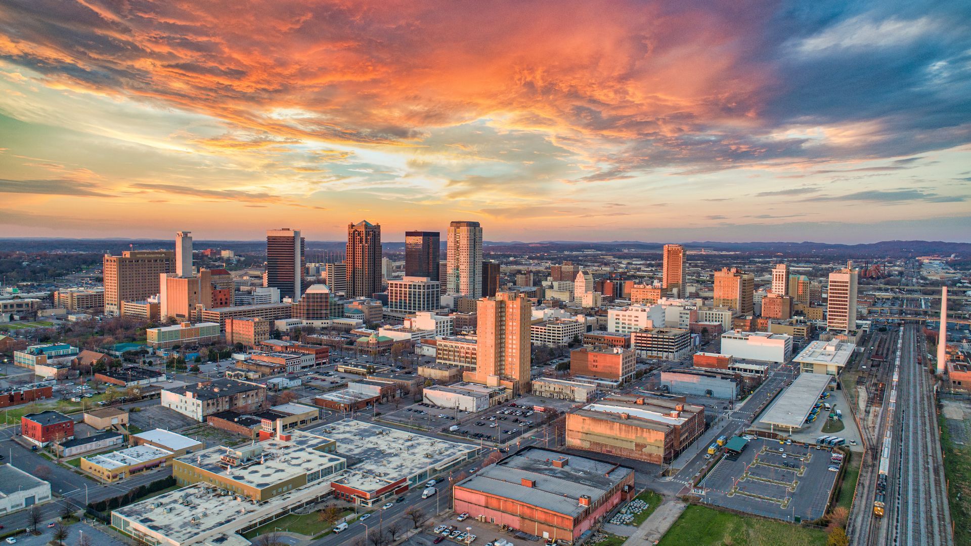 Aerial view of Birmingham, Alabama skyline at sunset, with colorful sky over city buildings.