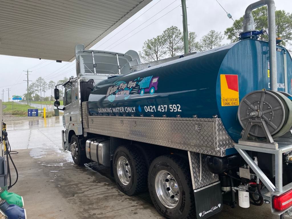 Water tanker truck parked under a canopy at a gas station, hose reel visible. — Water TopUps Gympie in Pie Creek, QLD