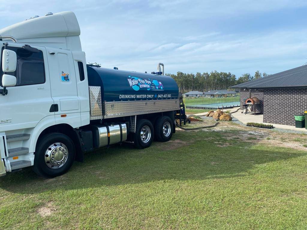 Septic tank truck parked on grass, hose connected to a house. Blue tank, white truck. — Water TopUps Gympie in Pie Creek, QLD
