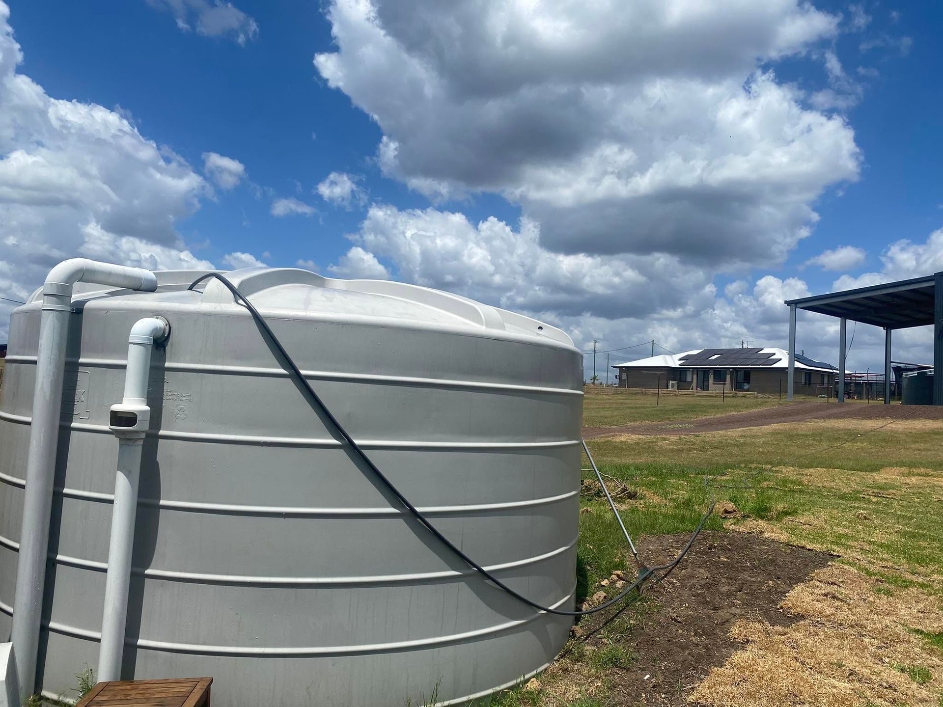 Large white water tank beside a dirt path under a blue sky with clouds