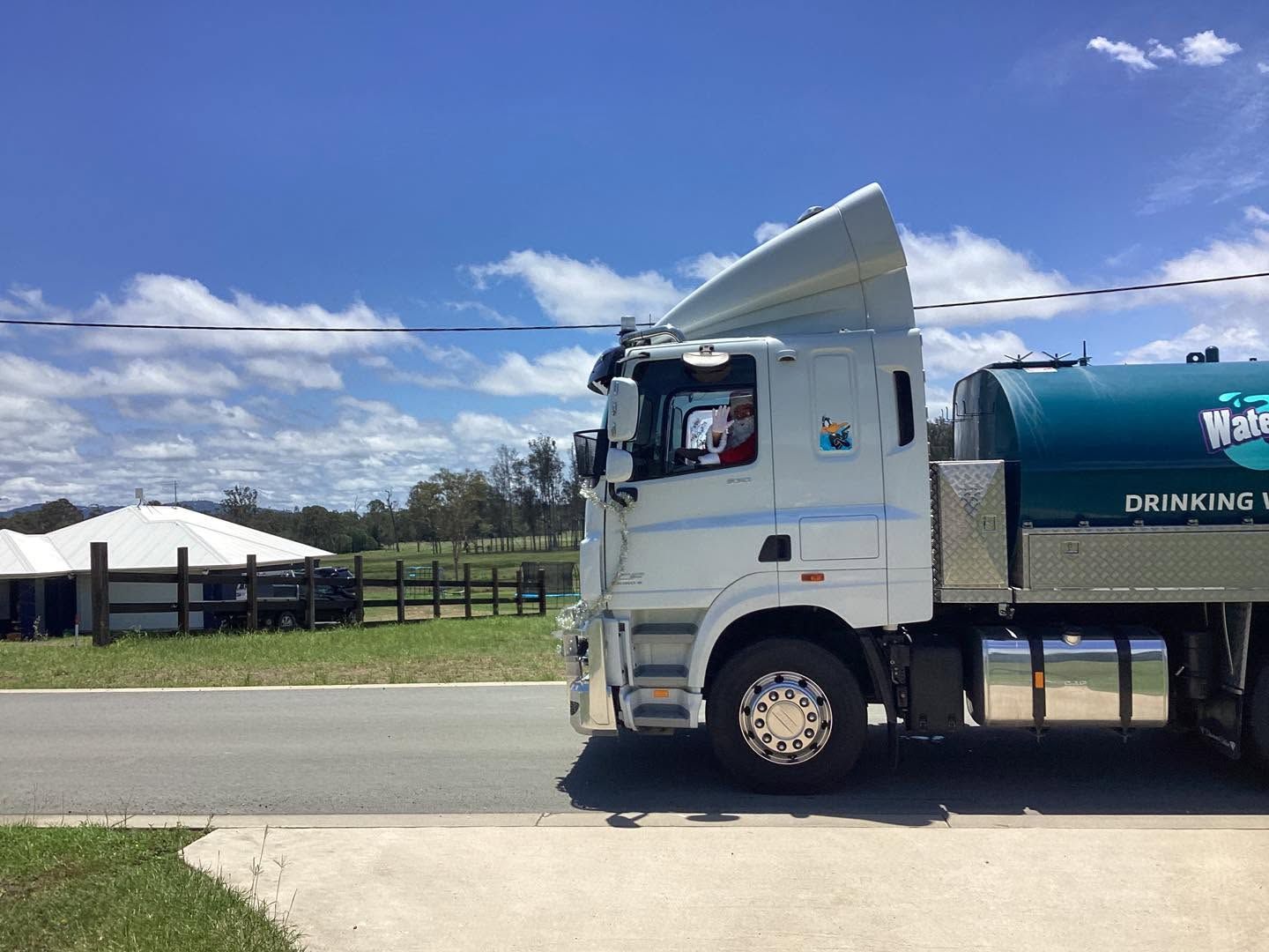 White tanker truck parked roadside on a sunny day with blue sky and tents in the background